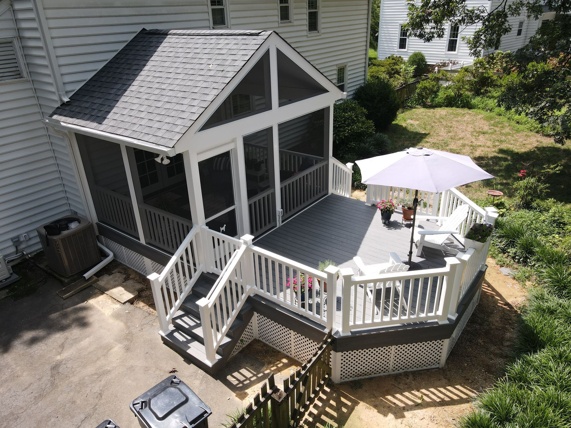 Backyard deck with screened porch, white railing, and patio umbrella beside a house