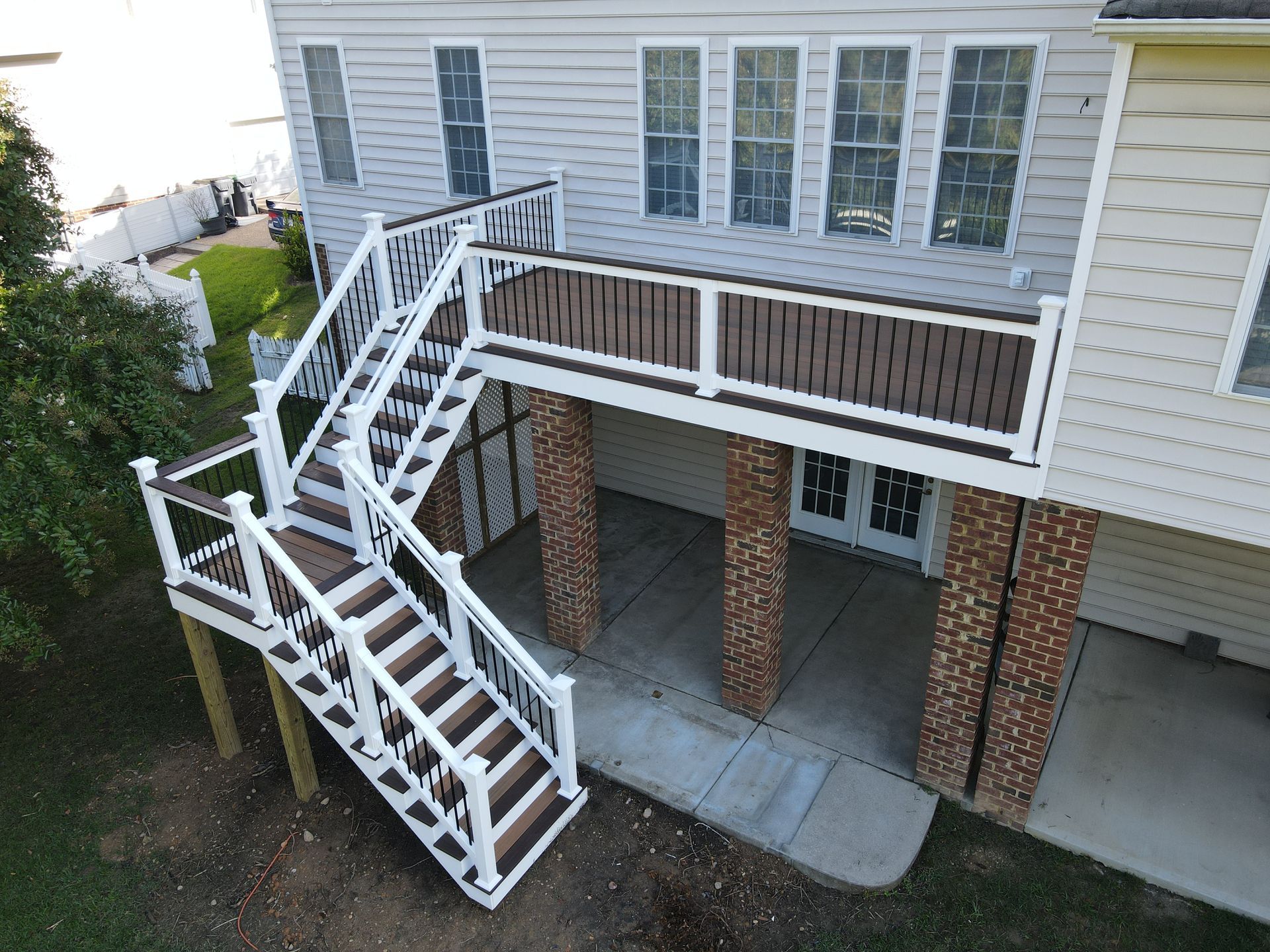 White exterior stairway and elevated walkway beside a brick apartment building with parked cars below