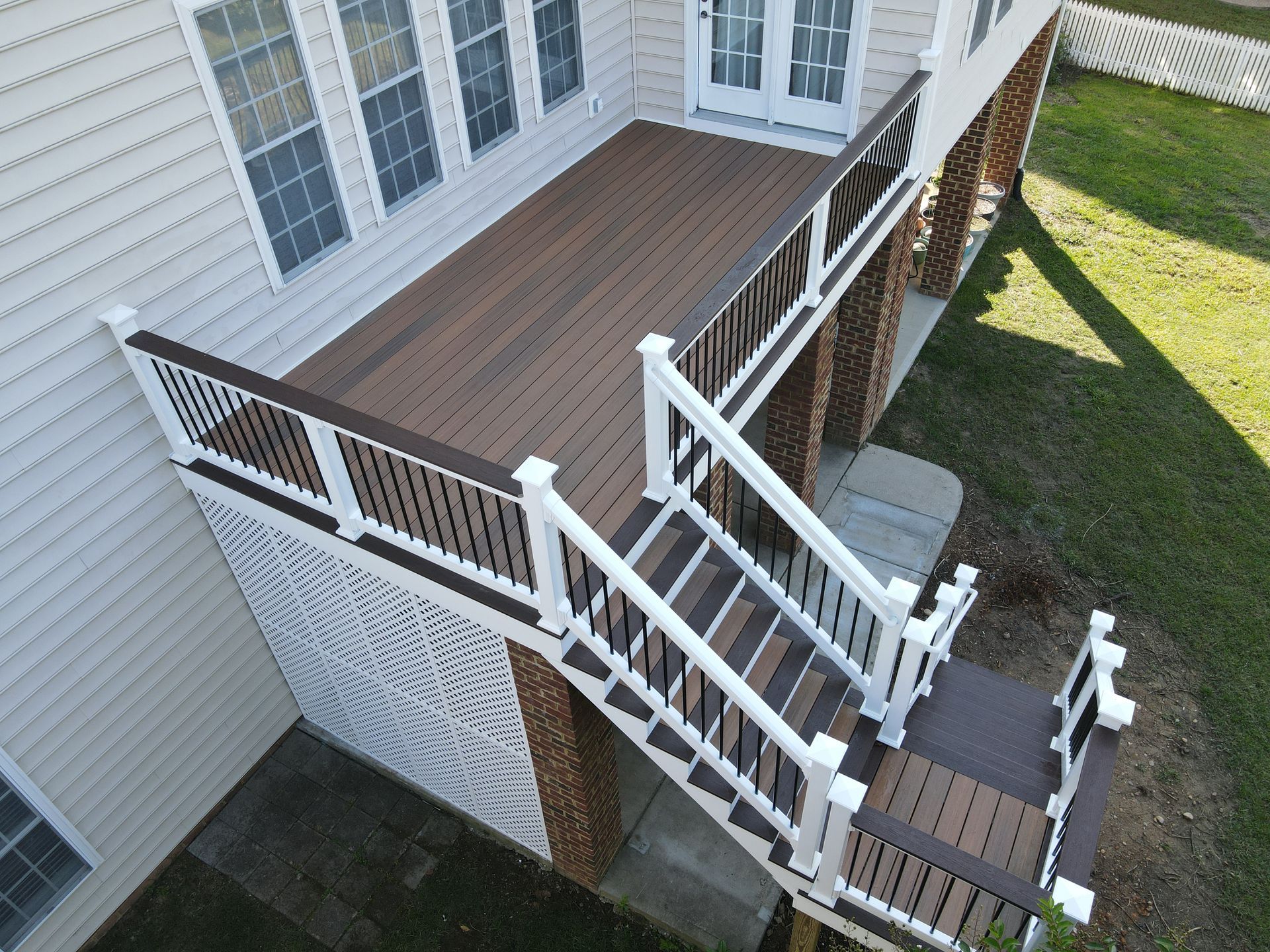 Raised wooden deck with white railings and stairs beside a house, viewed from above