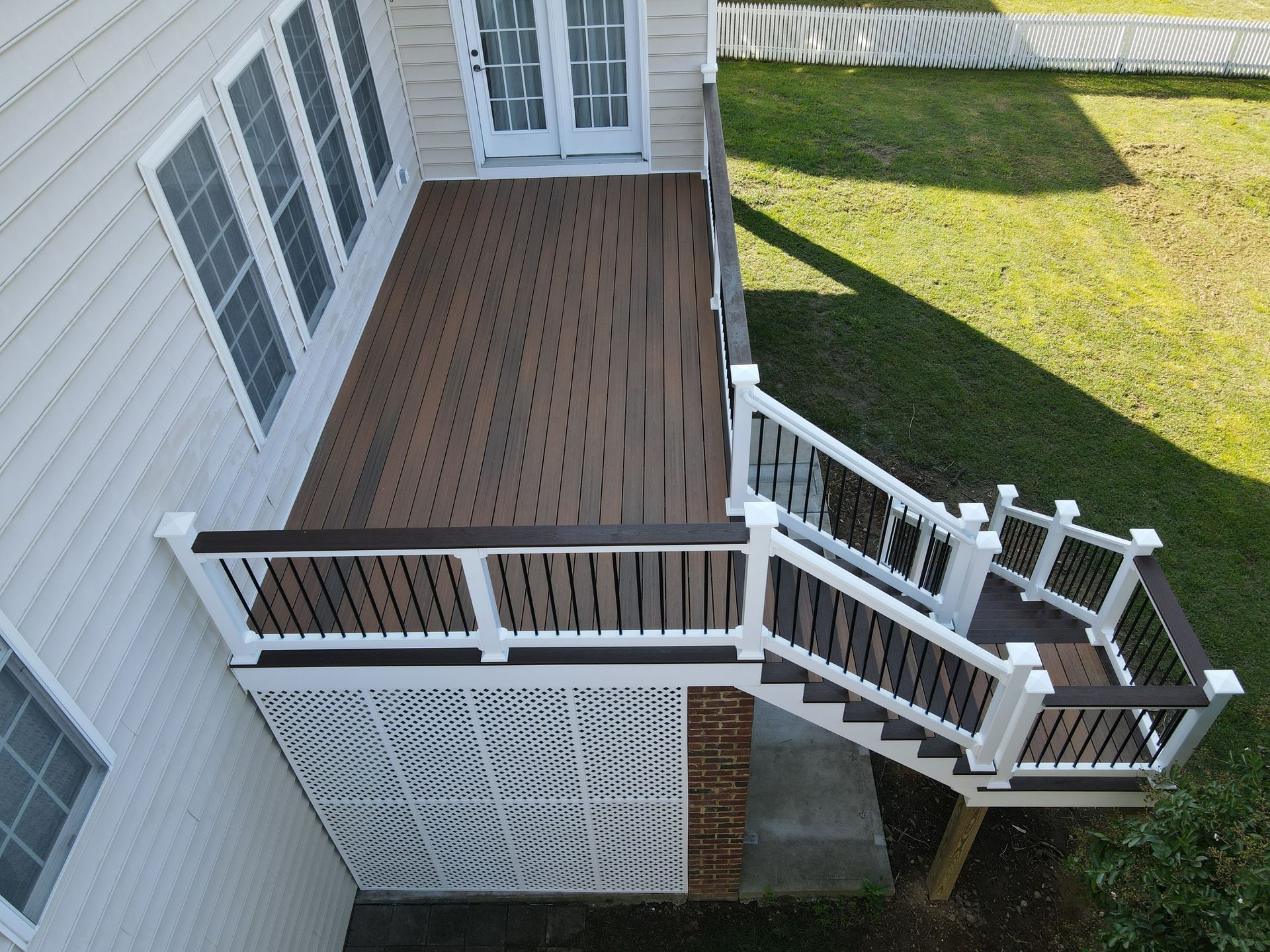 Small wooden deck with white railing and steps beside a house, overlooking a grassy yard.