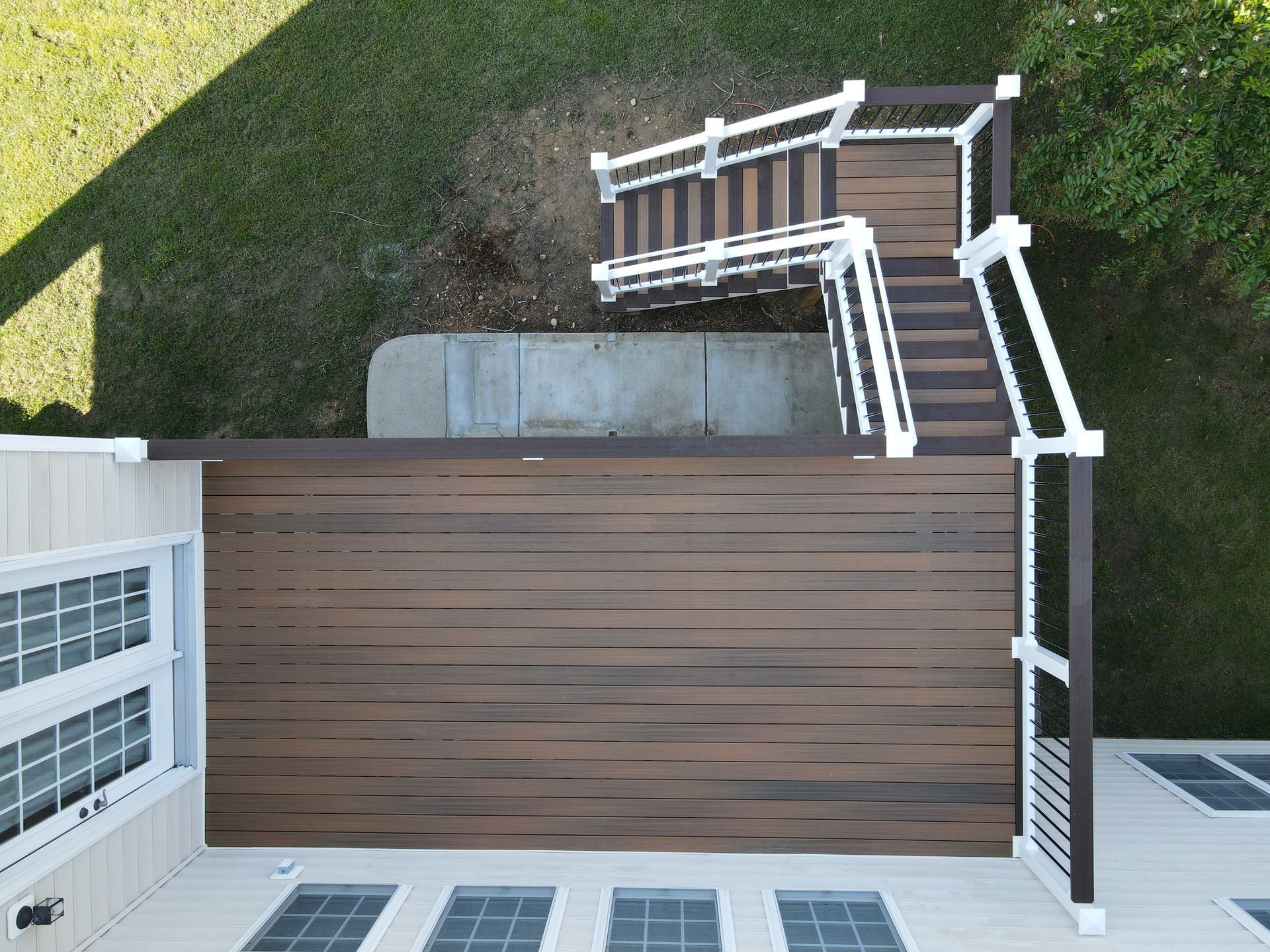 Top-down view of a wooden deck with white railings and stairs beside a grassy yard.