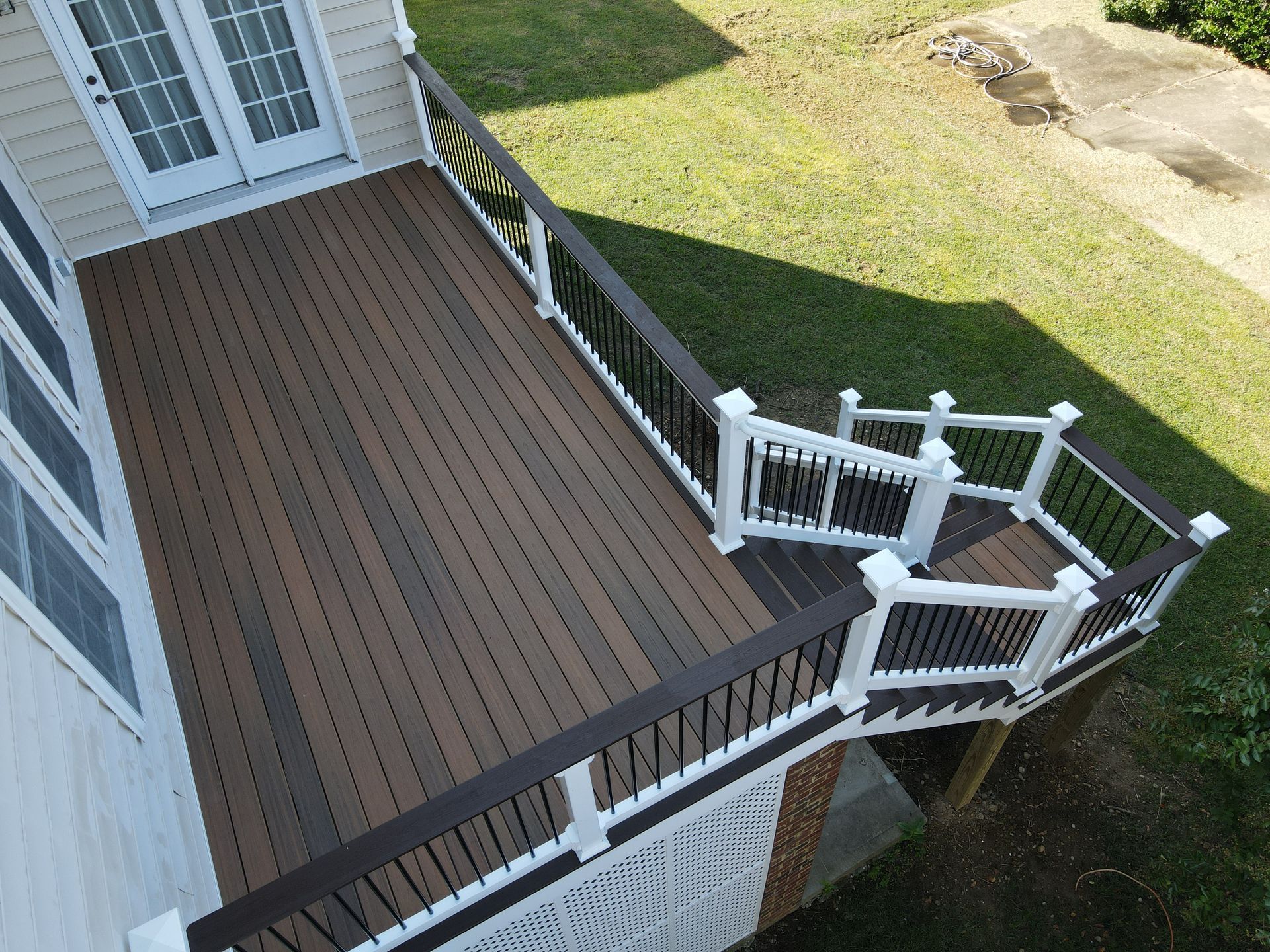 Wooden deck with white railings and stairs beside a house, viewed from above