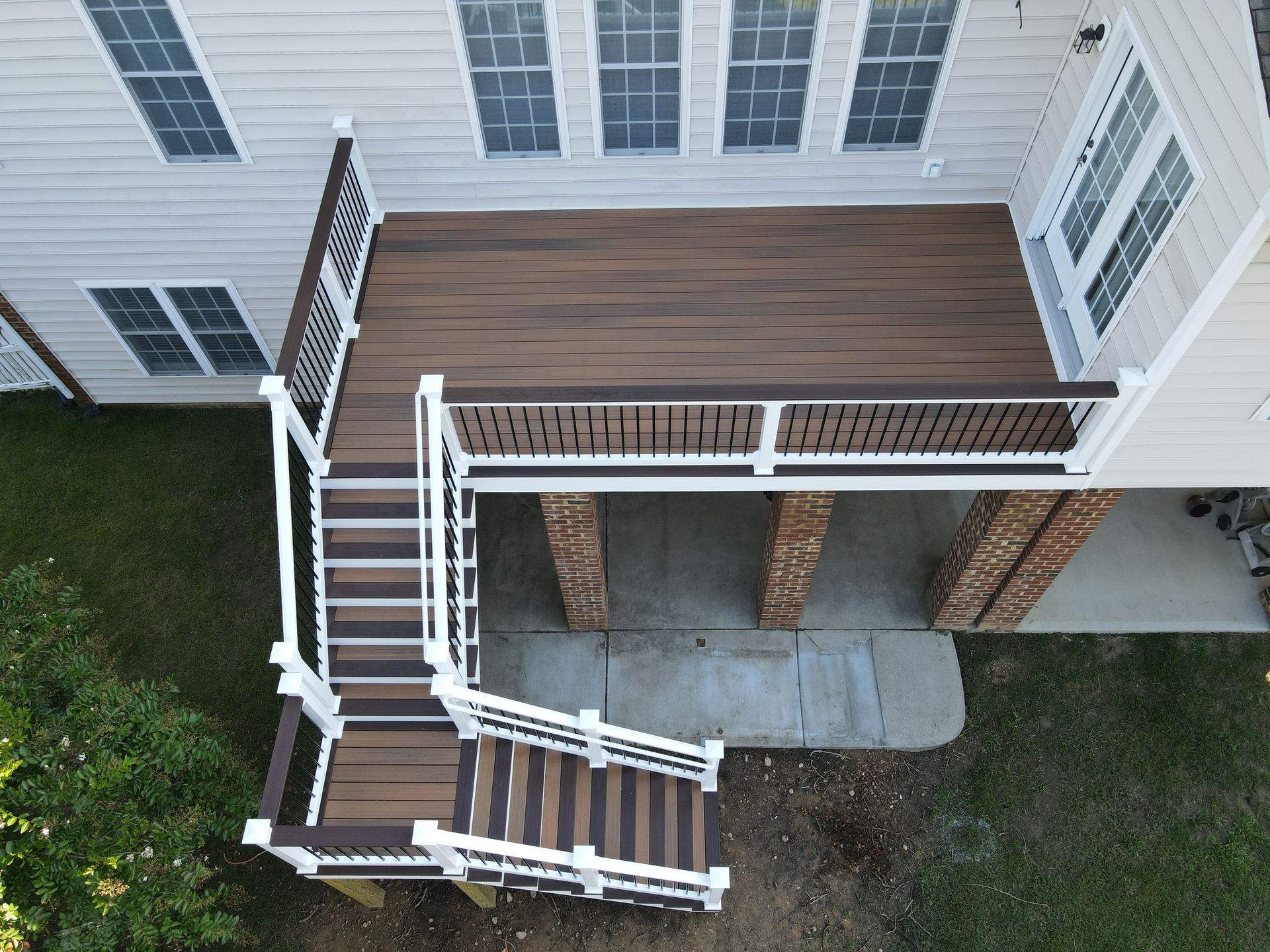Overhead view of a white house deck with brown wood flooring, stairs, and brick support columns