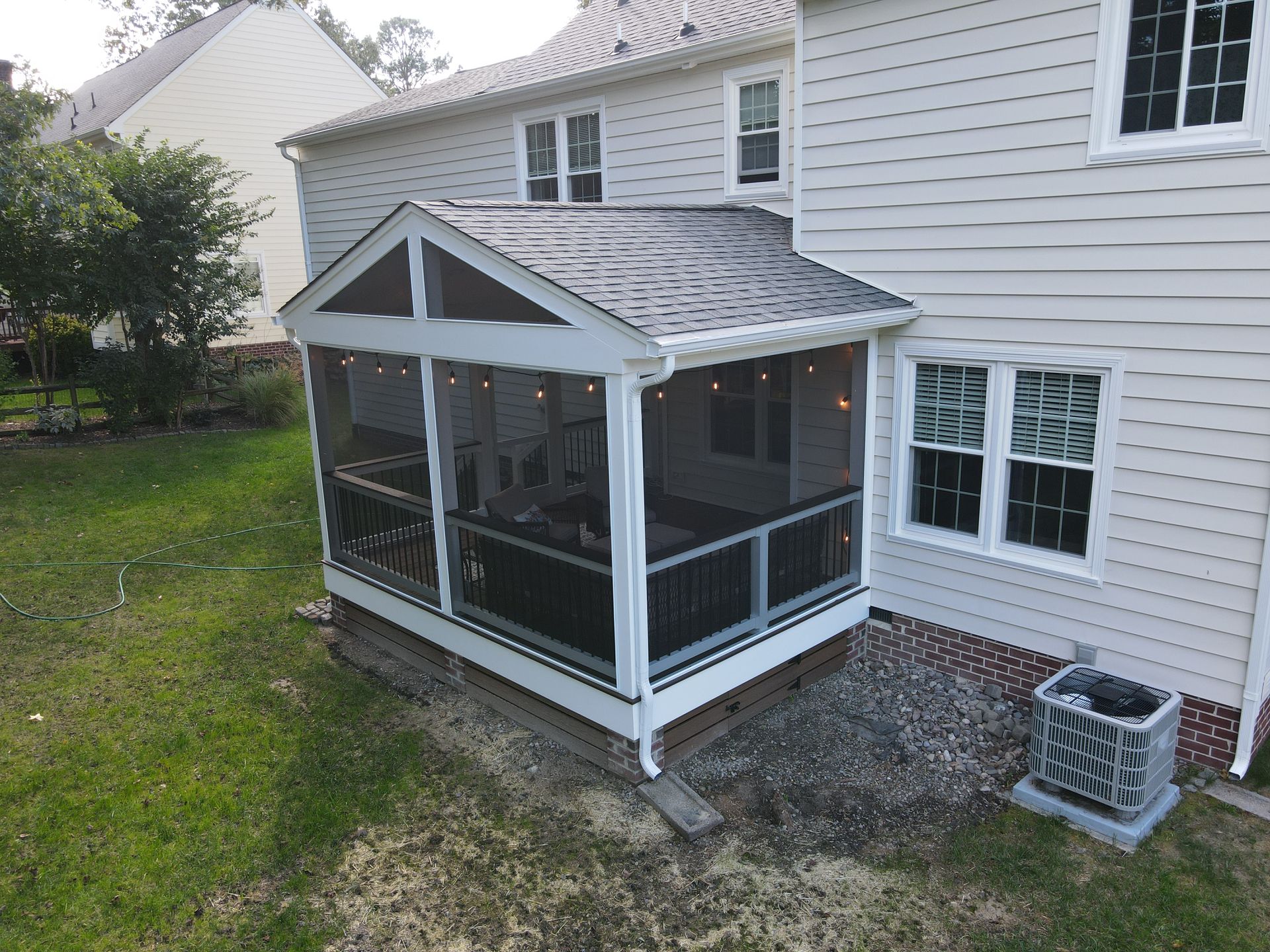 Backyard screened porch attached to a white house with gray roof shingles