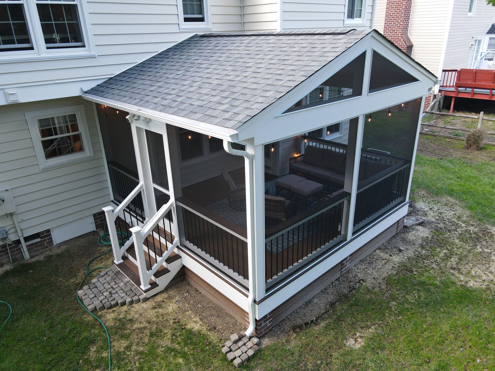 Small screened porch with a gabled roof and white trim attached to a house, on a grassy yard.