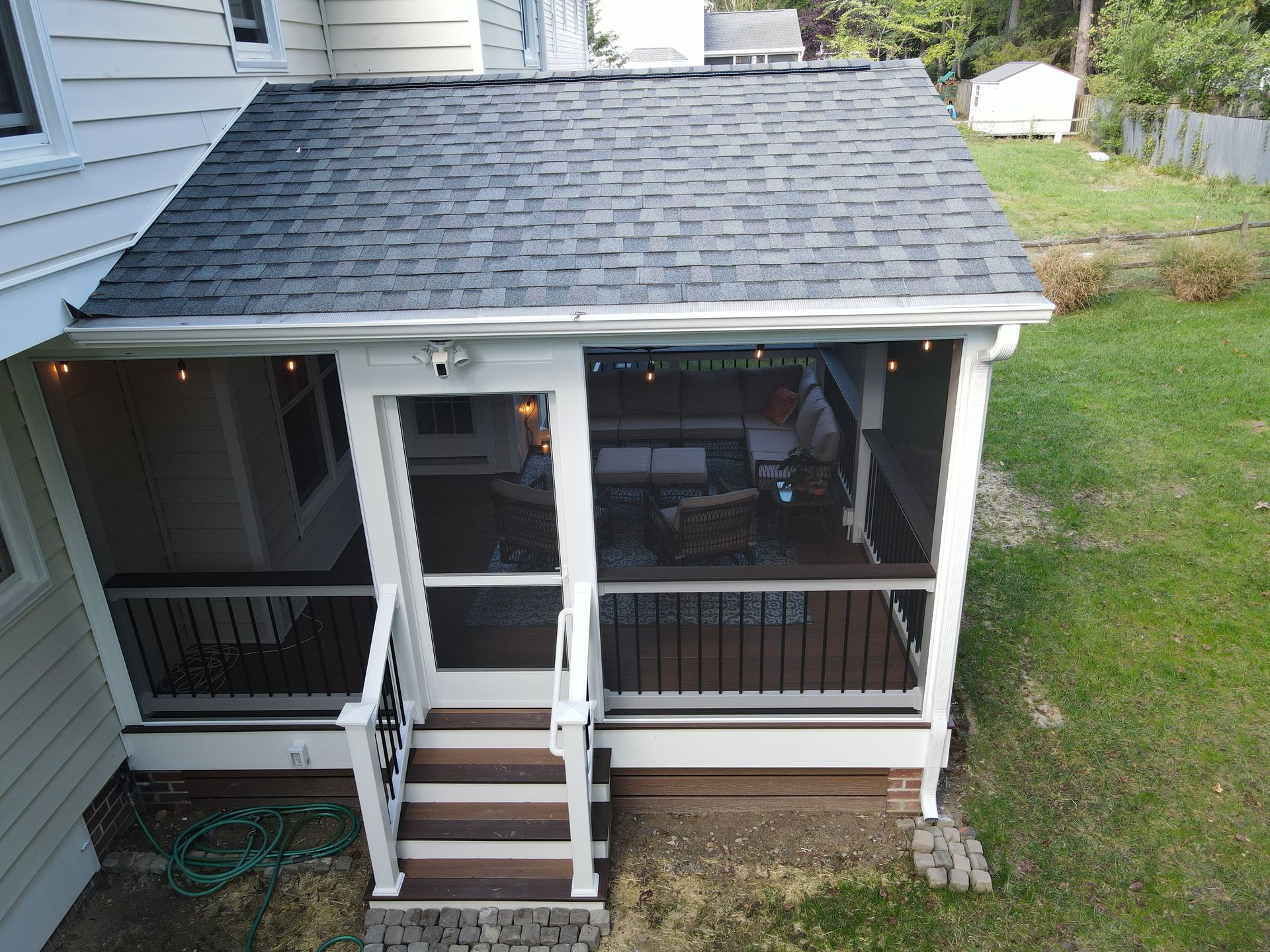 Small covered porch with white railings and dark roof on a house, showing steps and a lawn.