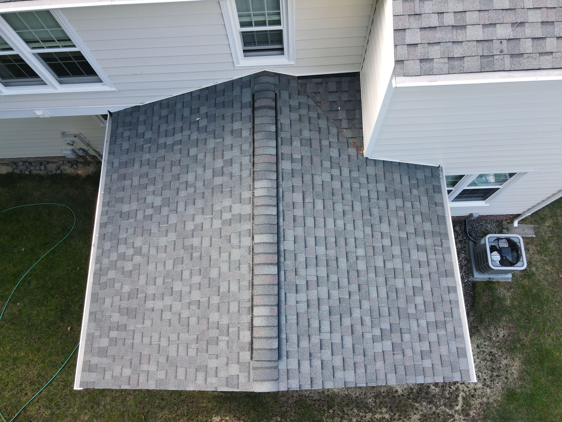 Overhead view of a gray shingled roof with a central ridge between two house sections