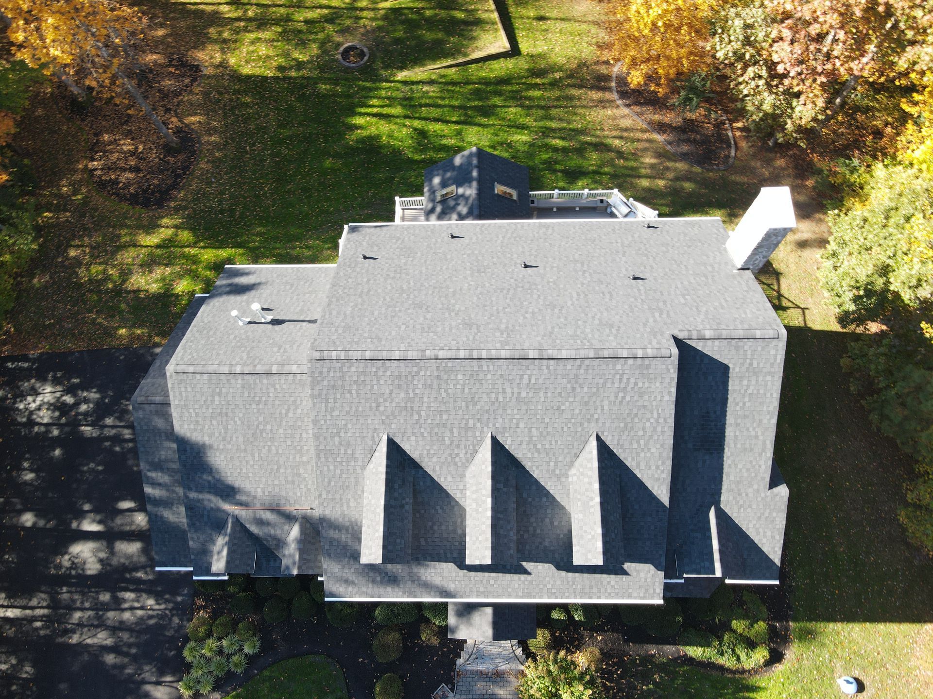Aerial view of a gray house with a steep roof, surrounded by trees and green lawn.