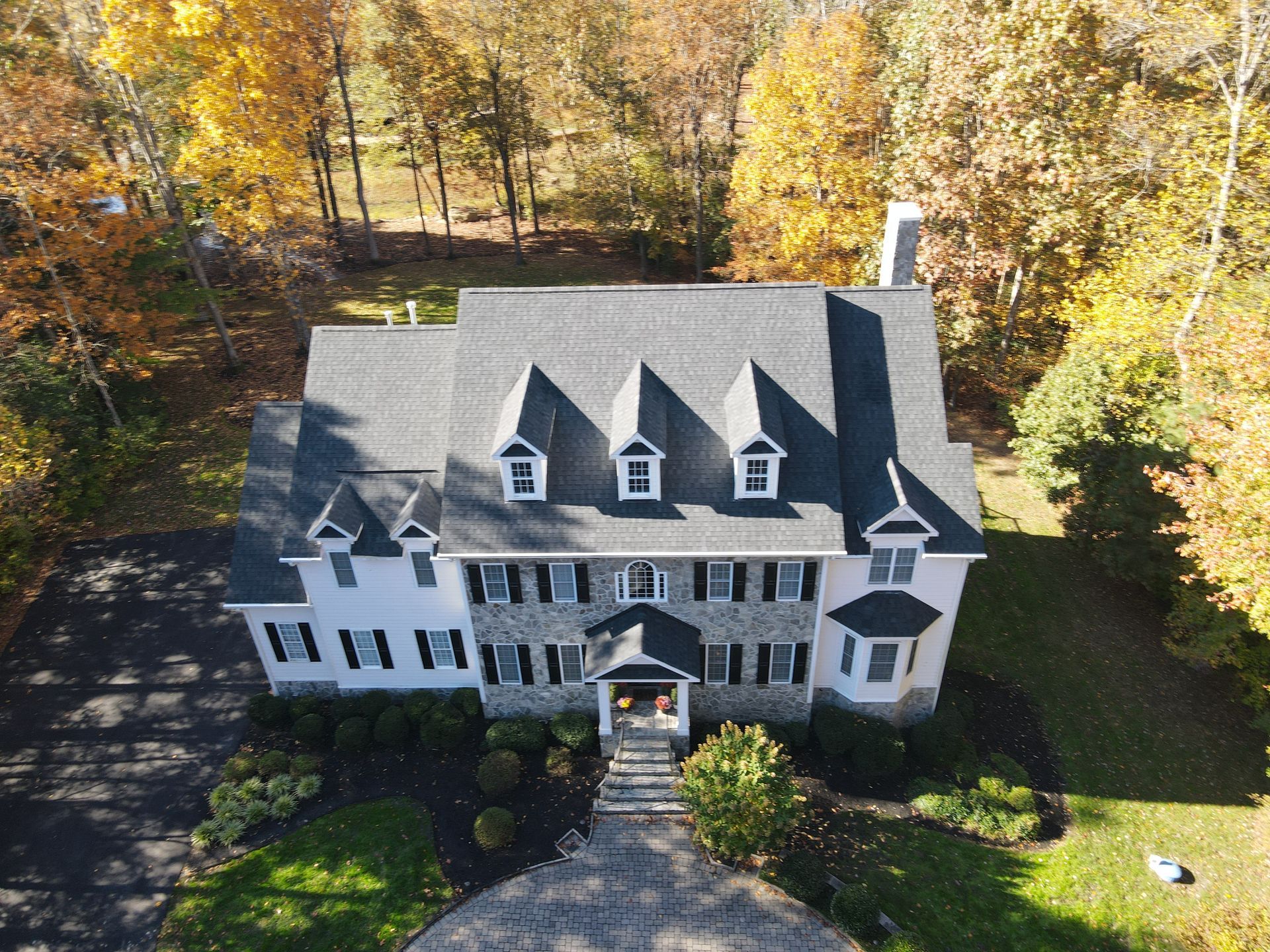 Aerial view of a large gray house with a steep roof, surrounded by autumn trees.