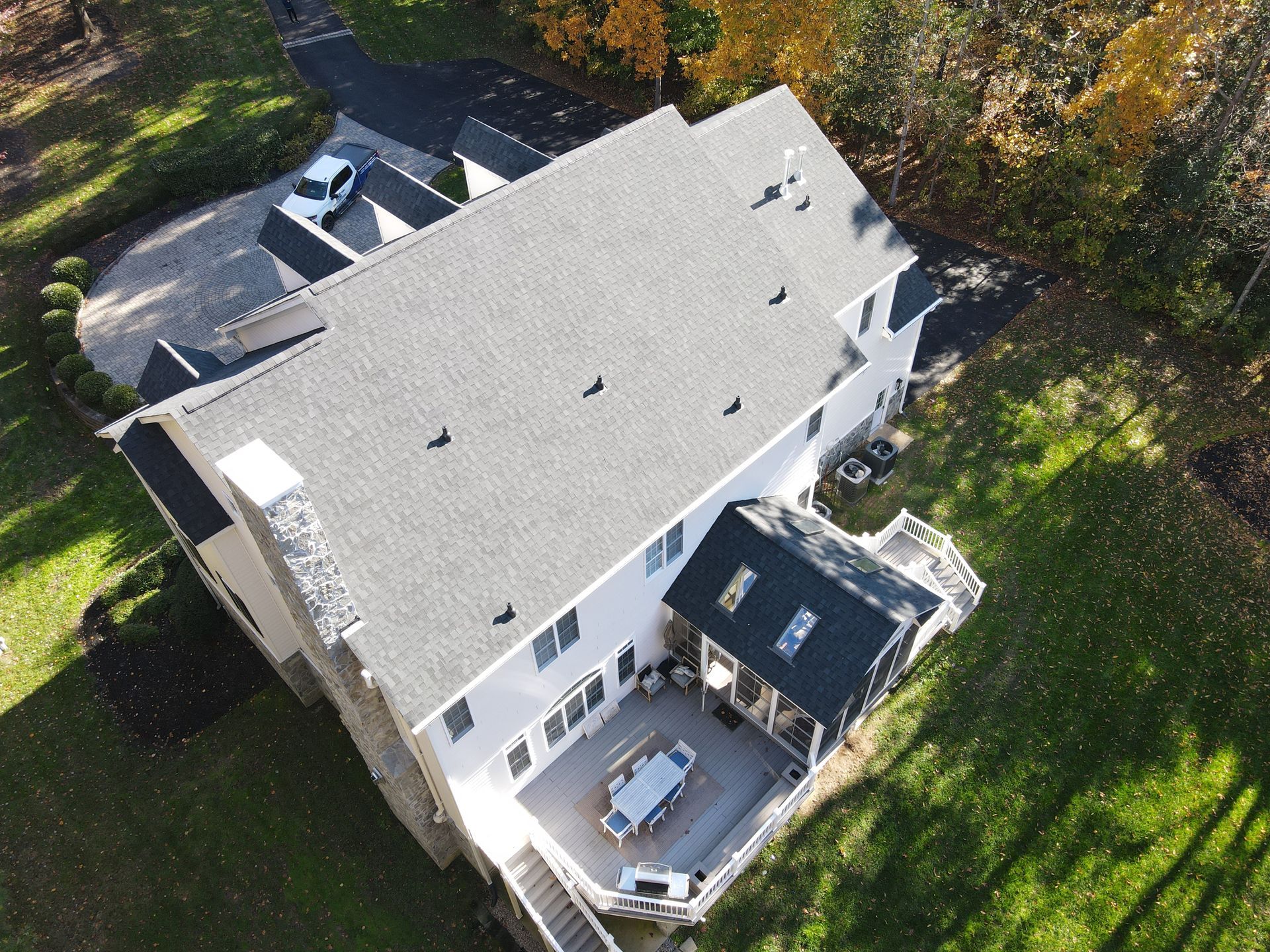 Aerial view of a white house with a gray roof, patio, and surrounding green yard.