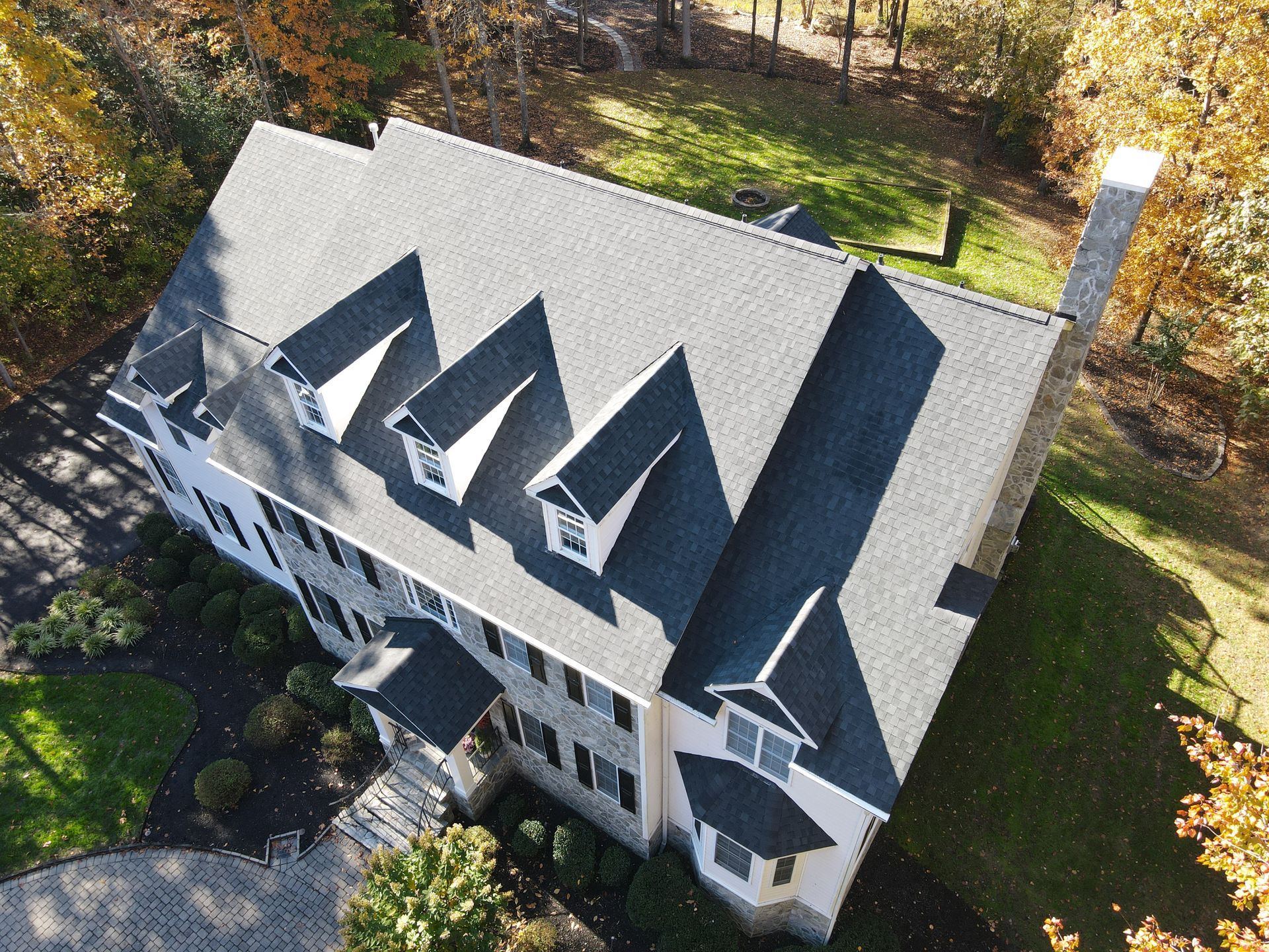 Aerial view of a white house with a dark gray roof and dormer windows surrounded by trees.
