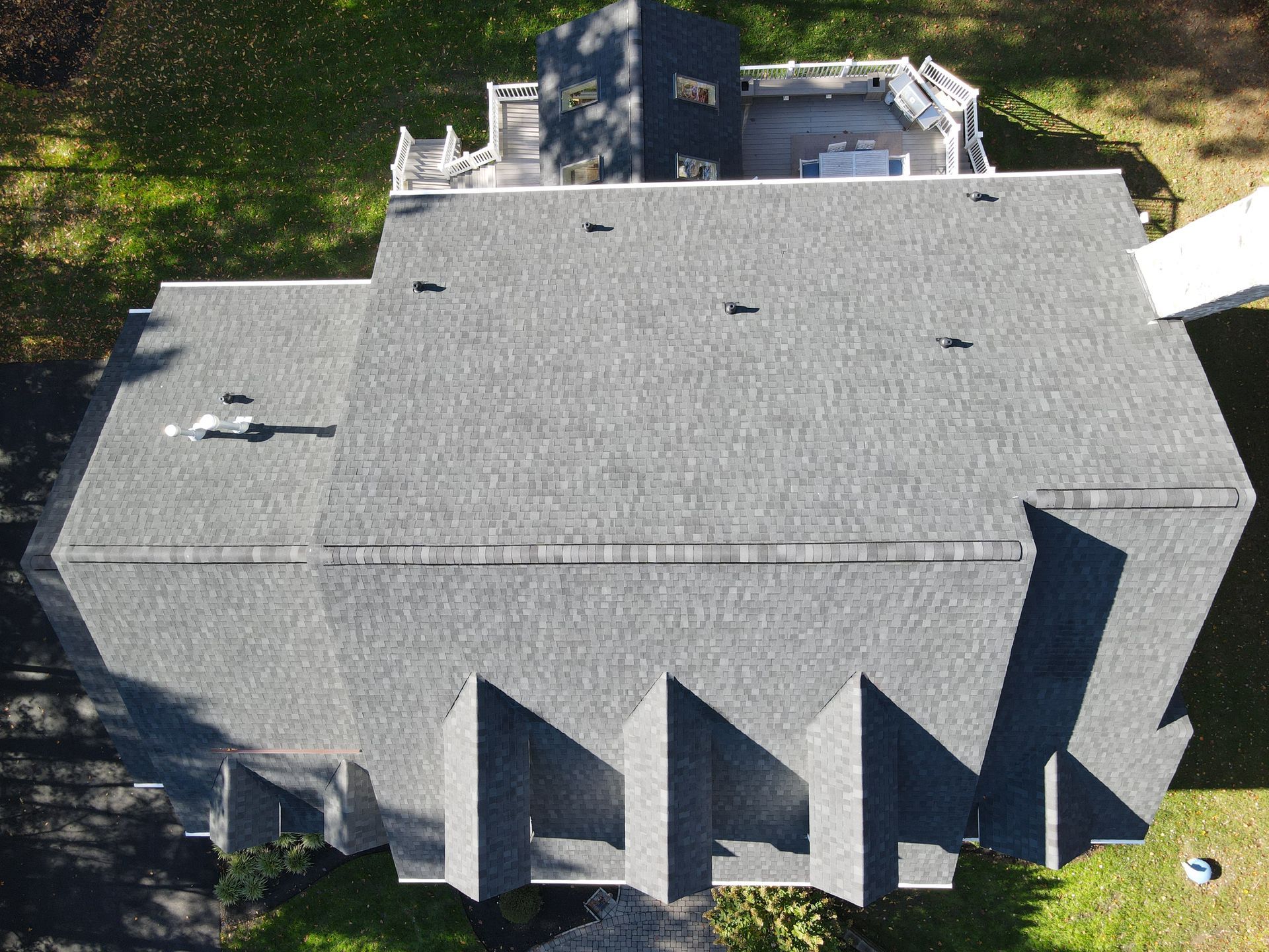 Aerial view of a gray shingled house roof with dormers and surrounding trees