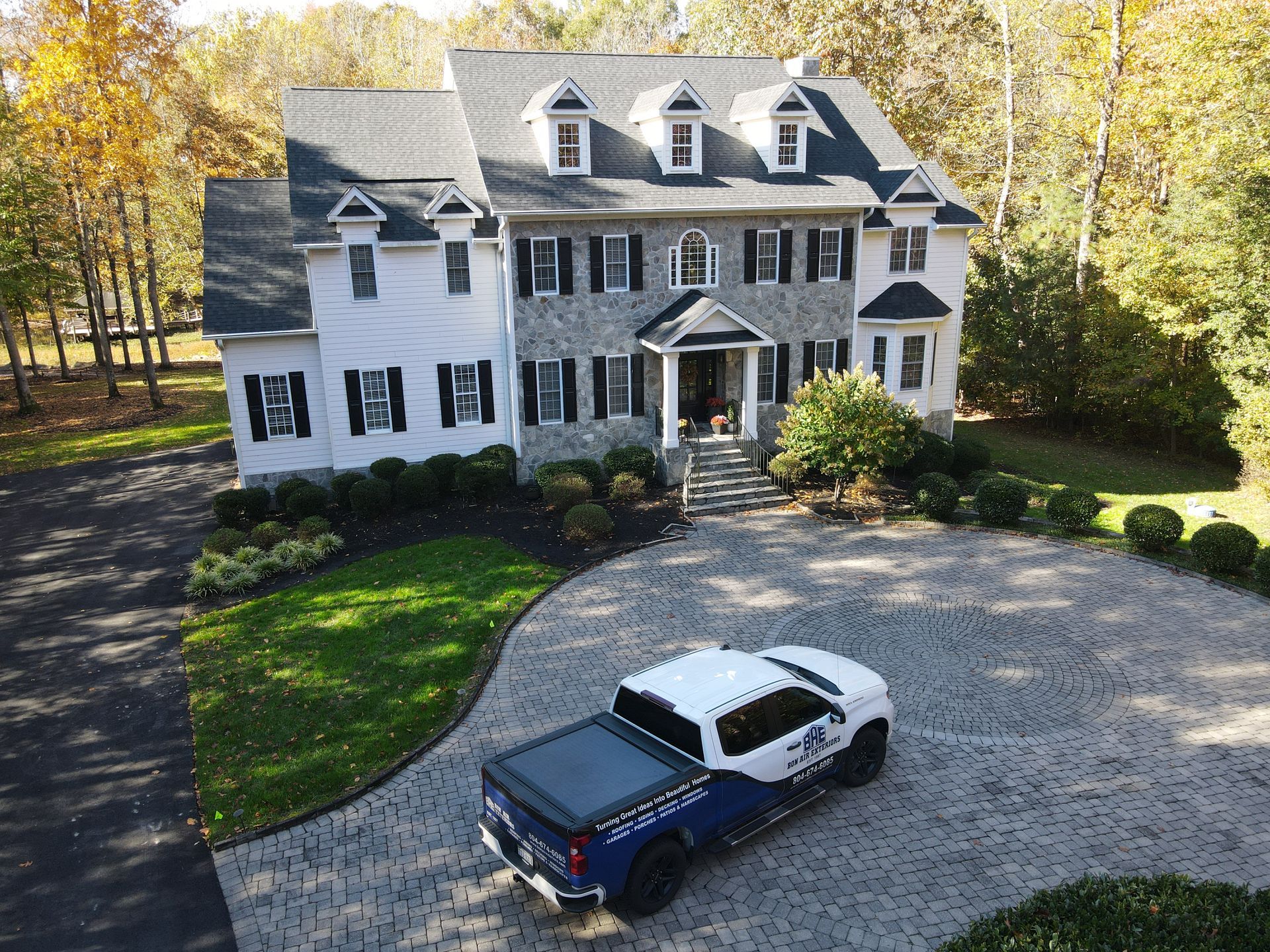 Large white colonial house with a gravel driveway and blue pickup truck in front, surrounded by autumn trees