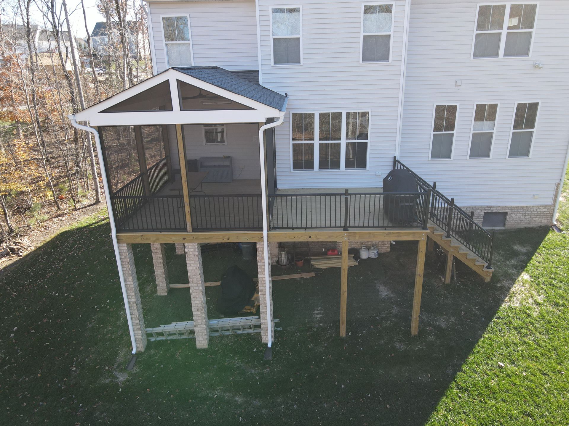 Back deck with covered porch, stairs, and wooden support posts beside a white house and grassy yard