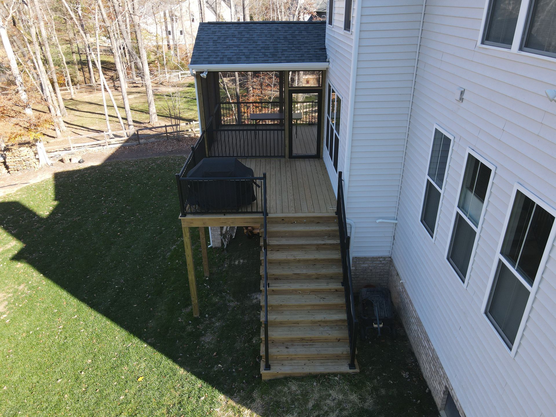 Backyard deck stairs beside a white house, with a screened porch and green lawn below