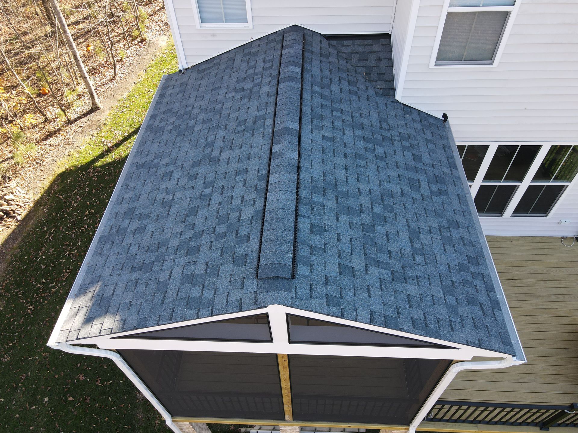 Aerial view of a blue shingled house roof with a screened porch and white siding.