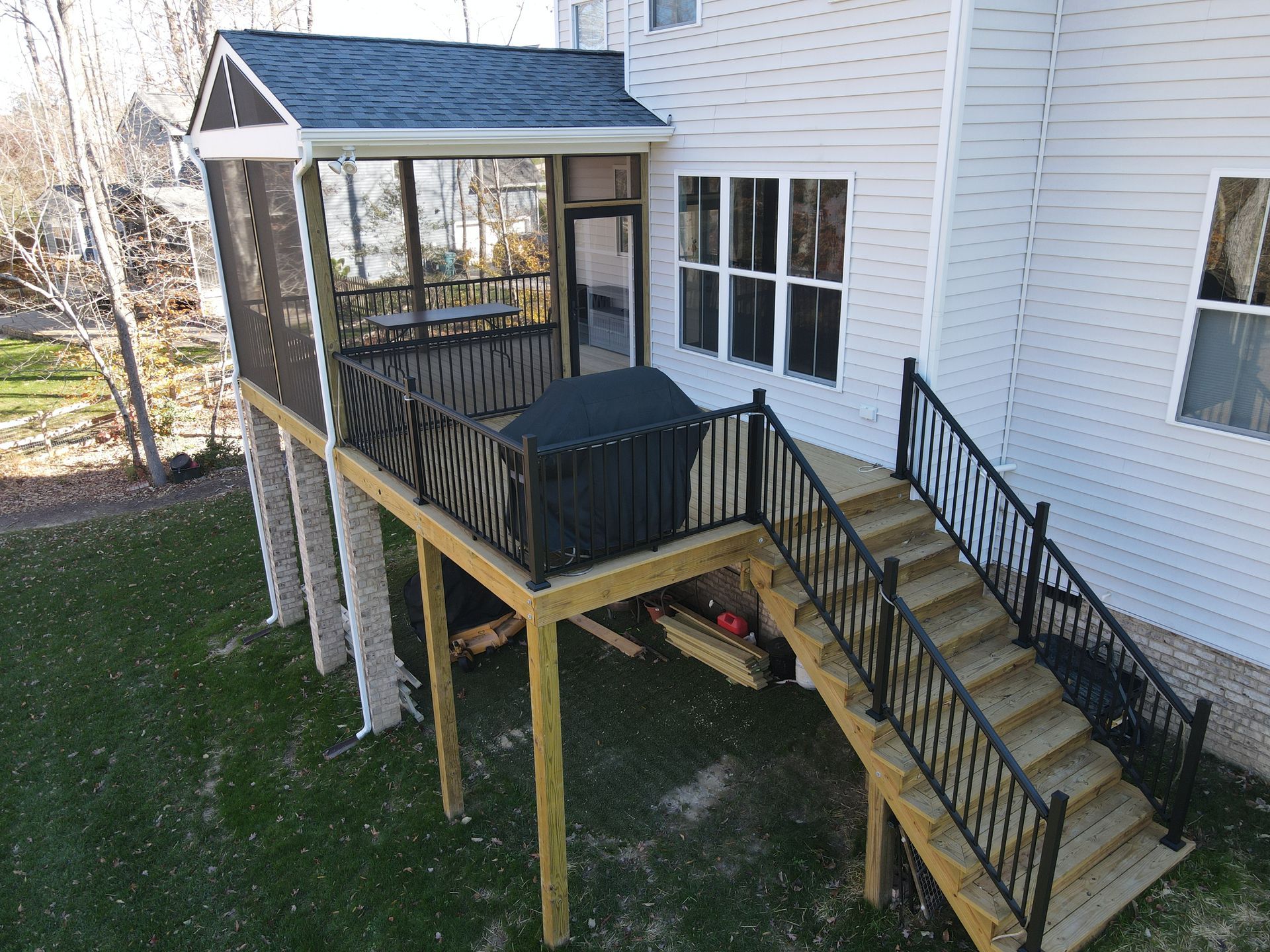 Elevated wooden deck with stairs and covered seating beside a white house