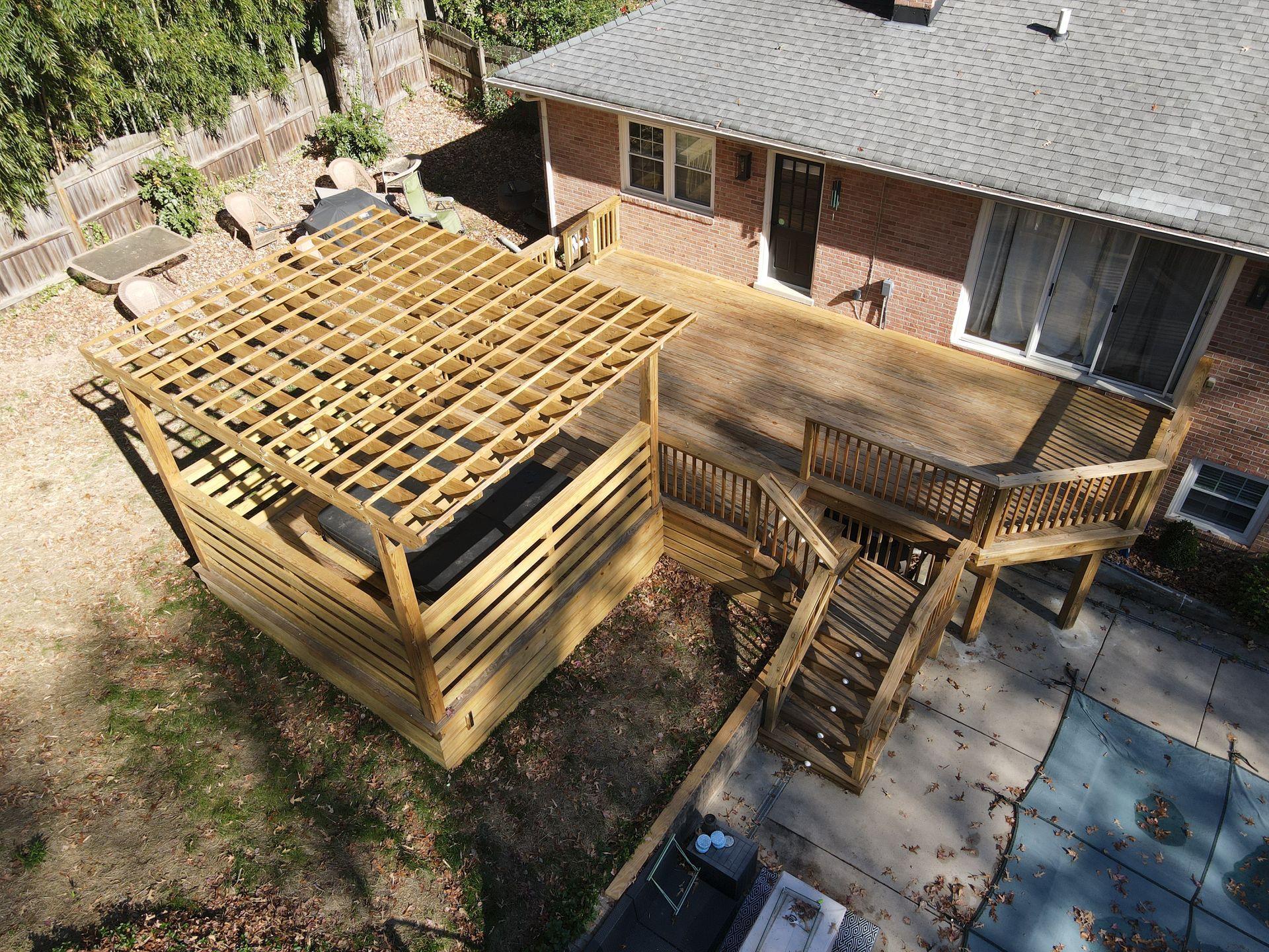 Backyard deck under construction with wooden railings, stairs, and exposed roof framing beside a brick house