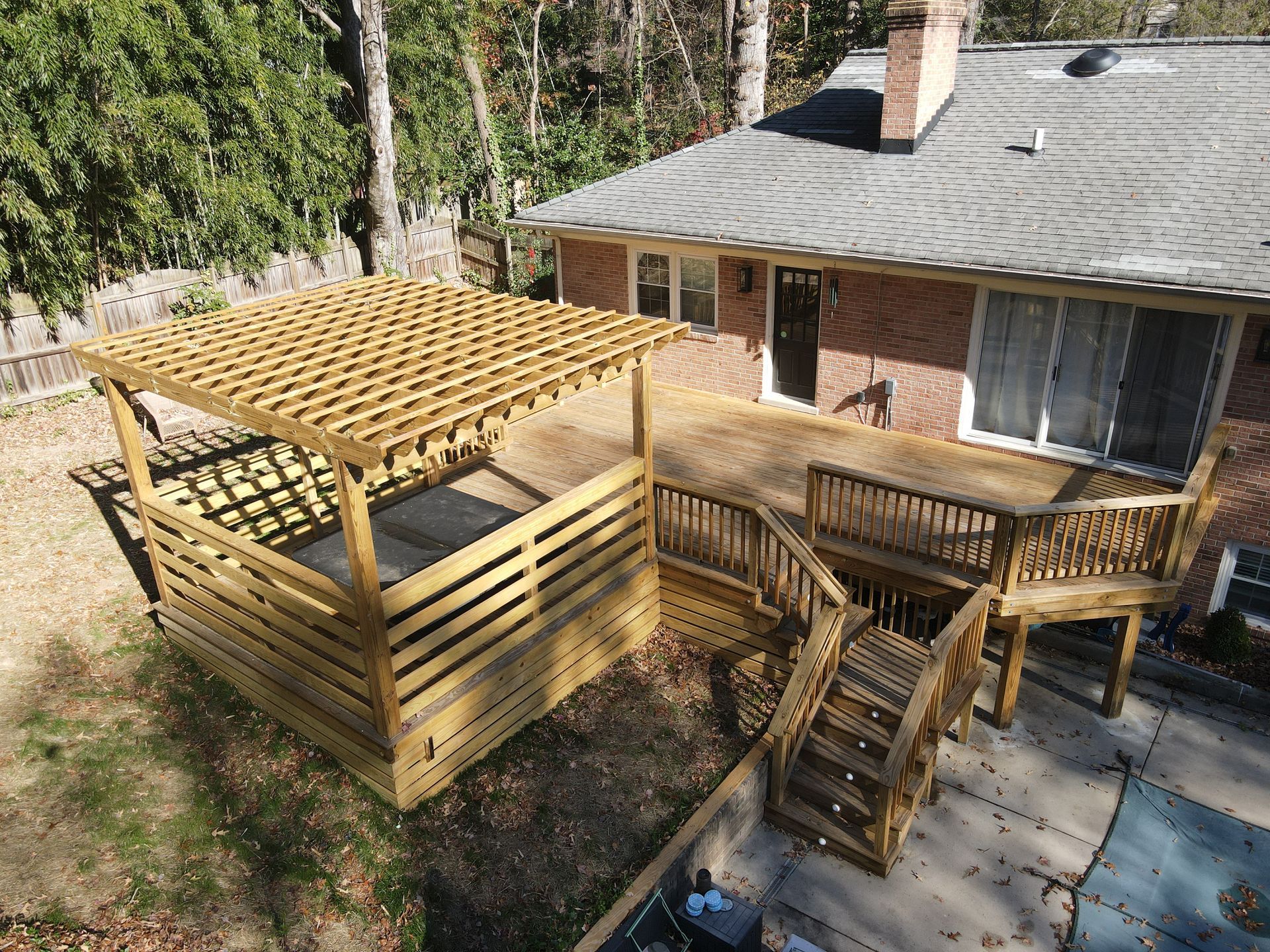 Wooden deck and staircase with pergola beside a house in a wooded yard