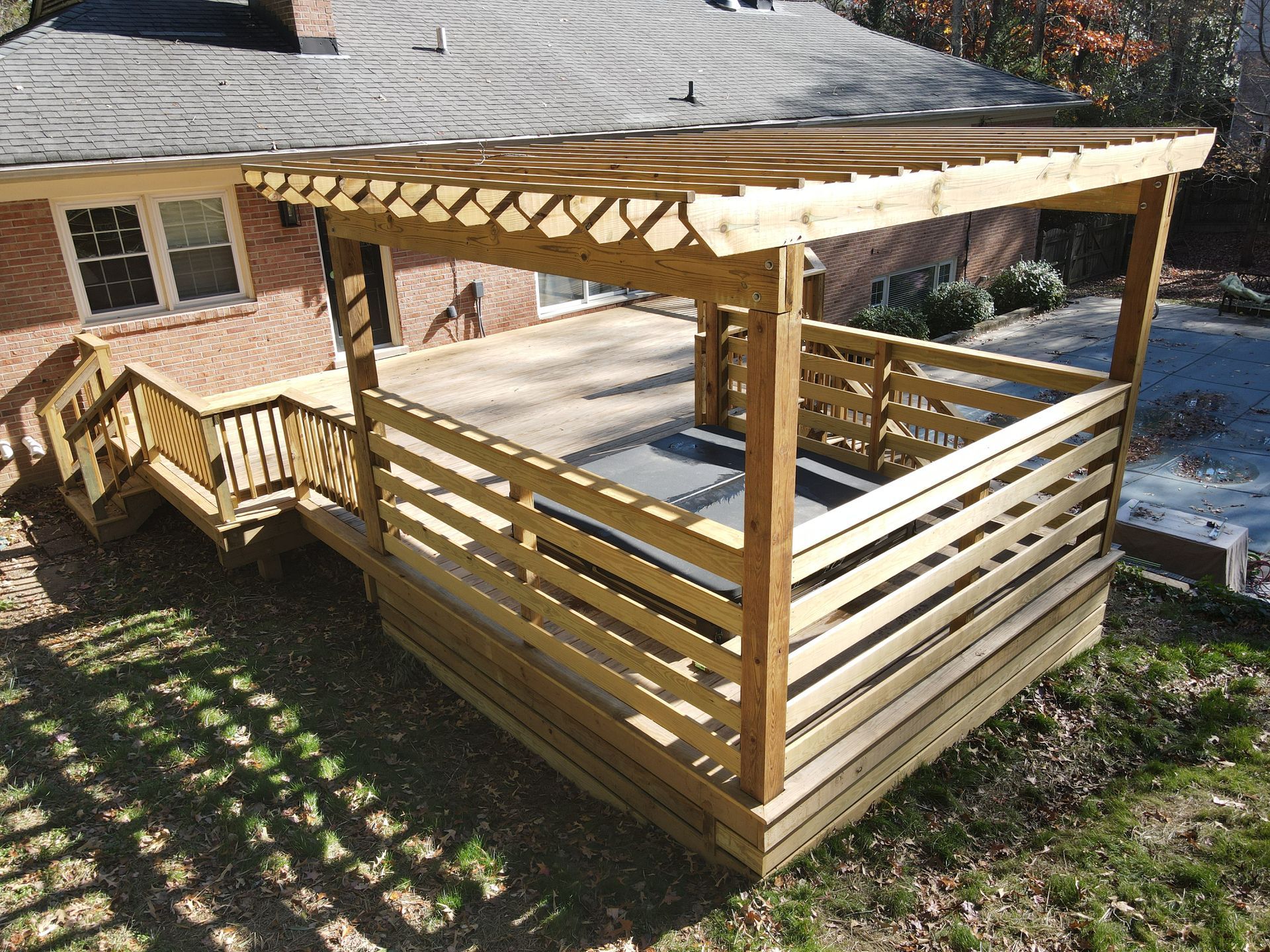 Wooden backyard deck with pergola and privacy slat railing beside a house