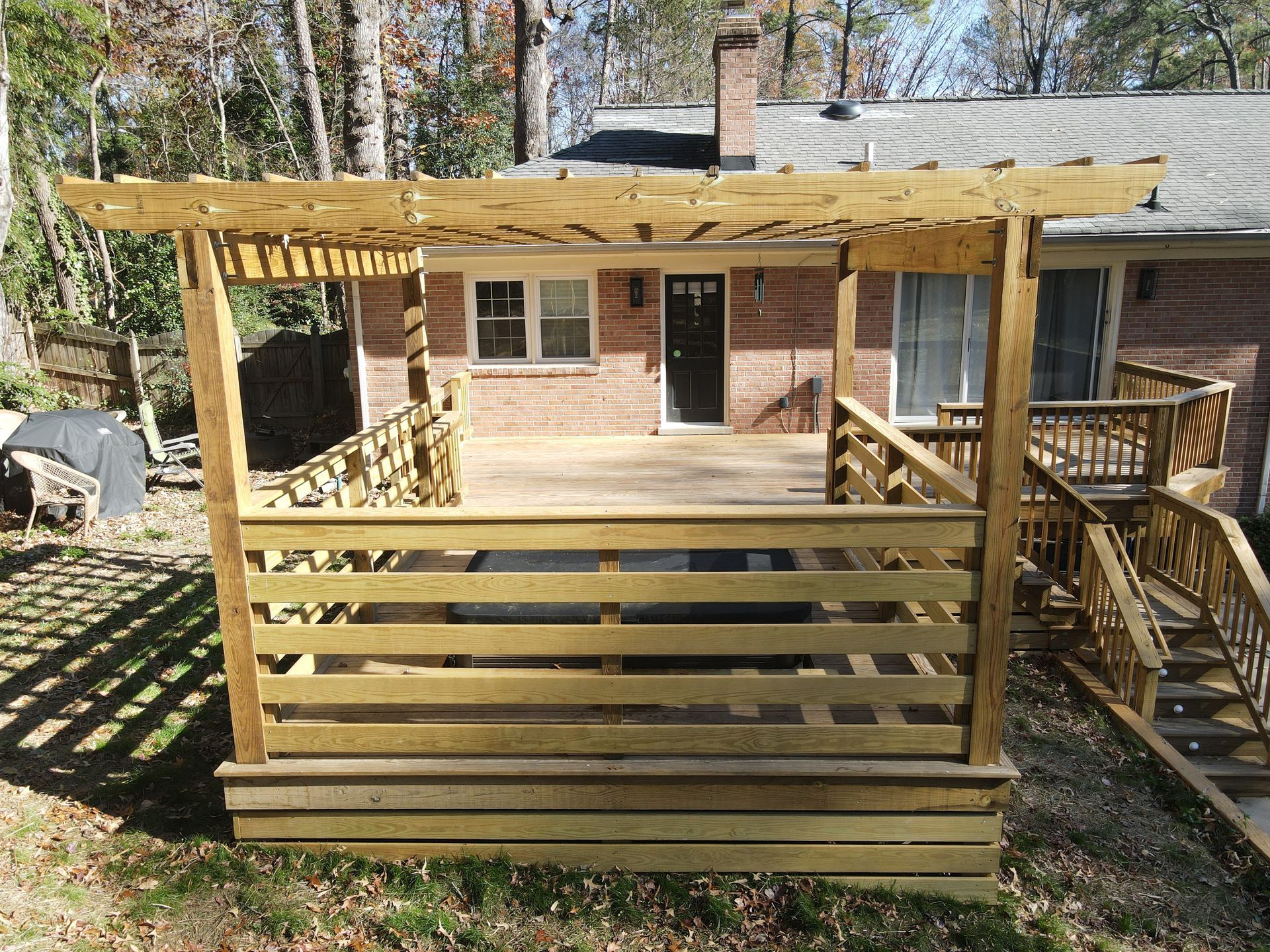 Wooden backyard deck with railing and stairs in front of a brick house
