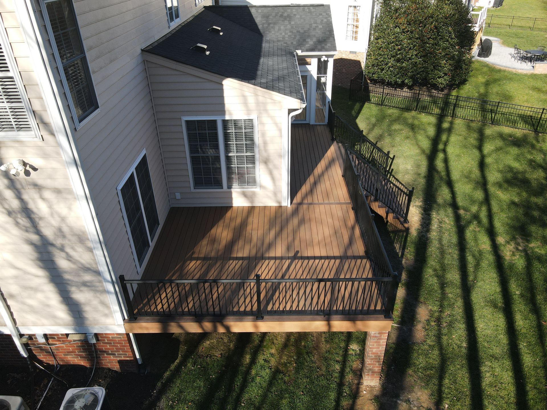 Aerial view of a house with a wooden back deck and steps beside a grassy yard.