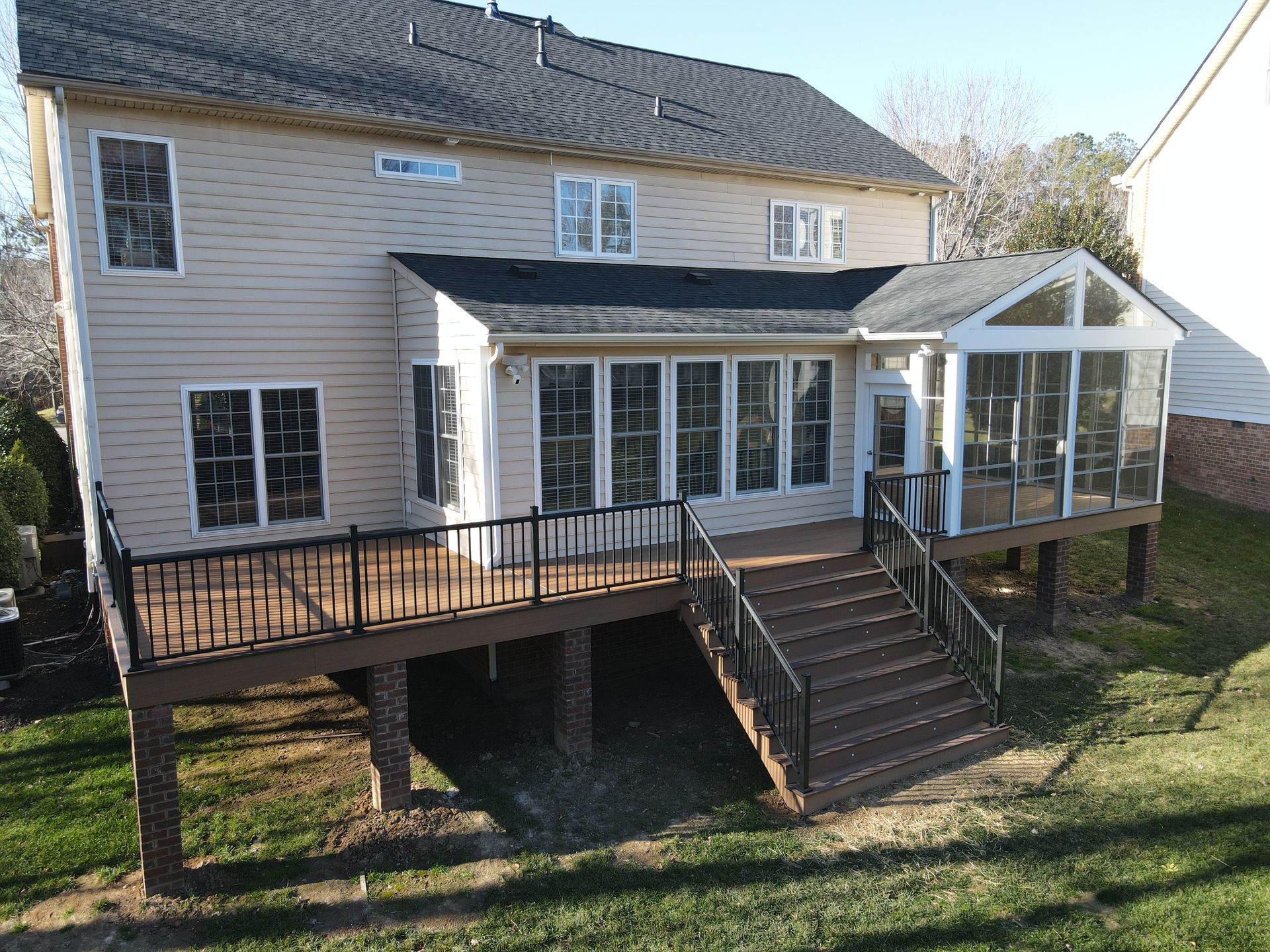 Back deck with stairs, railings, and a sunroom attached to a beige two-story house