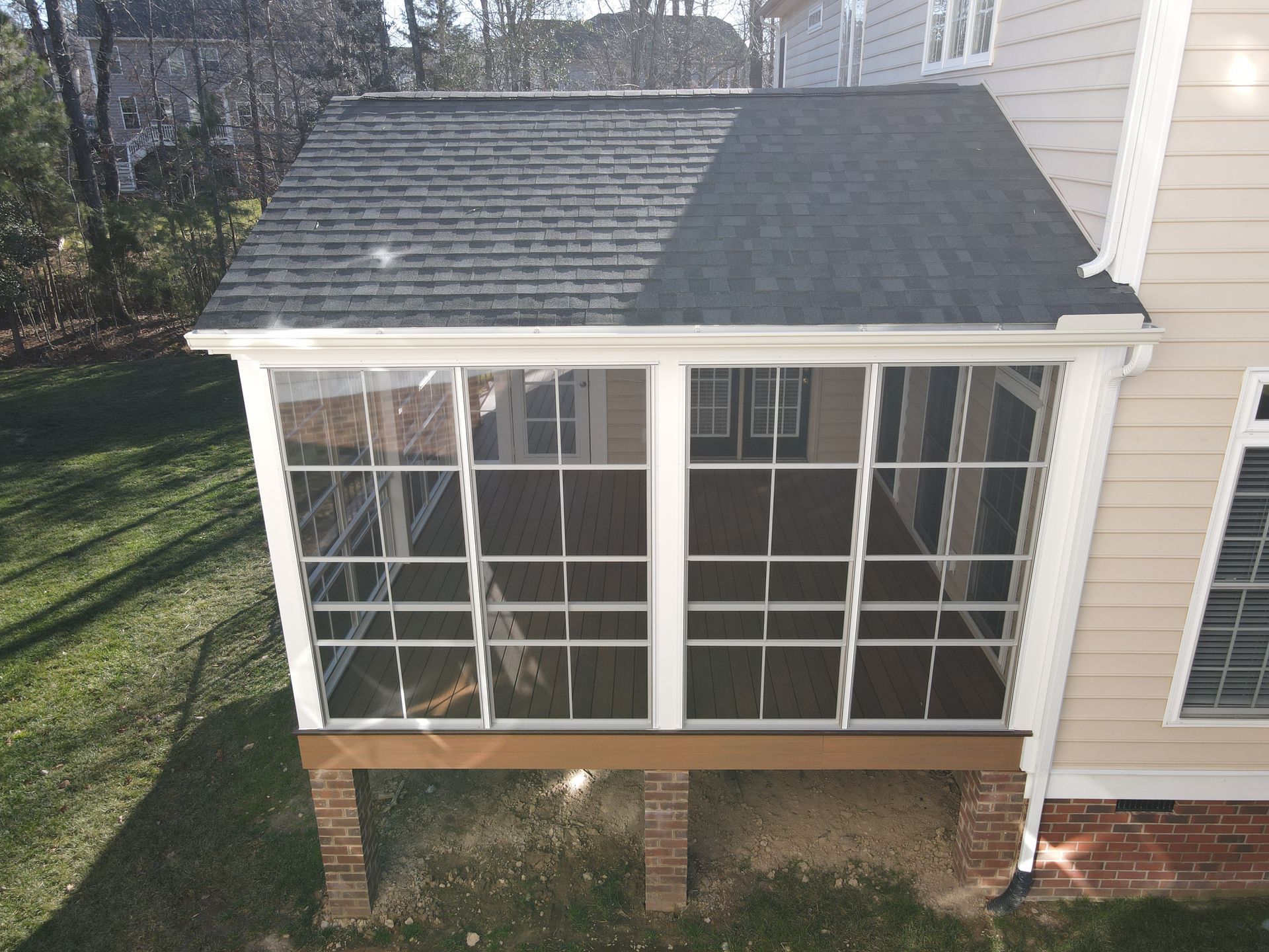 Screened porch with white-framed windows and a gray shingled roof attached to a beige house.
