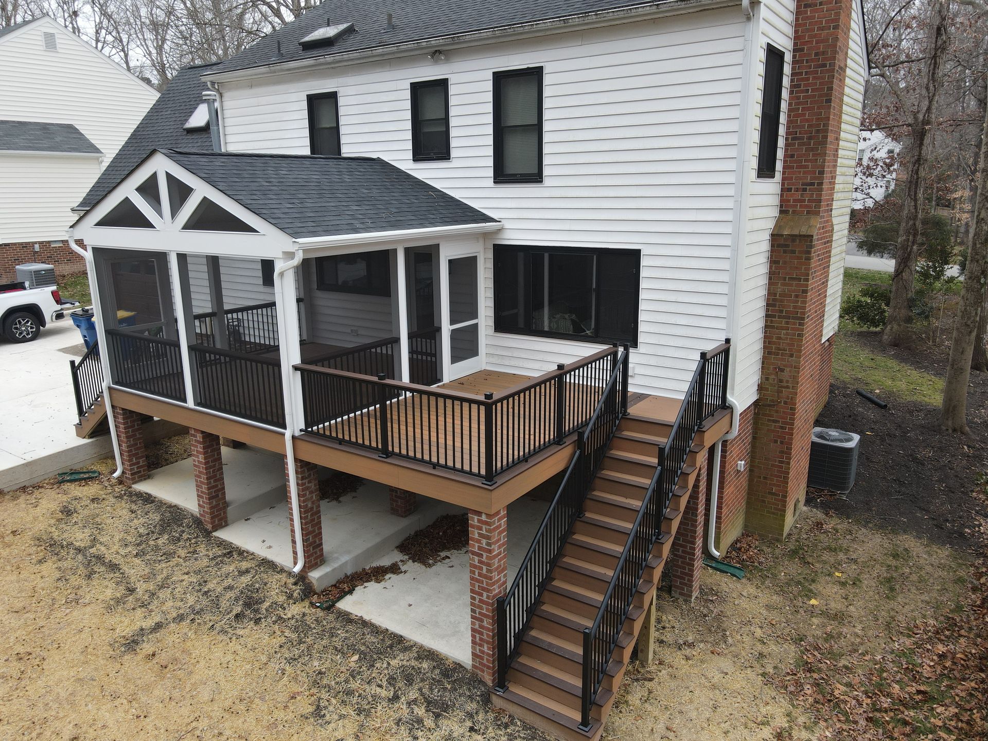 Back deck and dual staircases on a white two-story house with black railings and covered porch