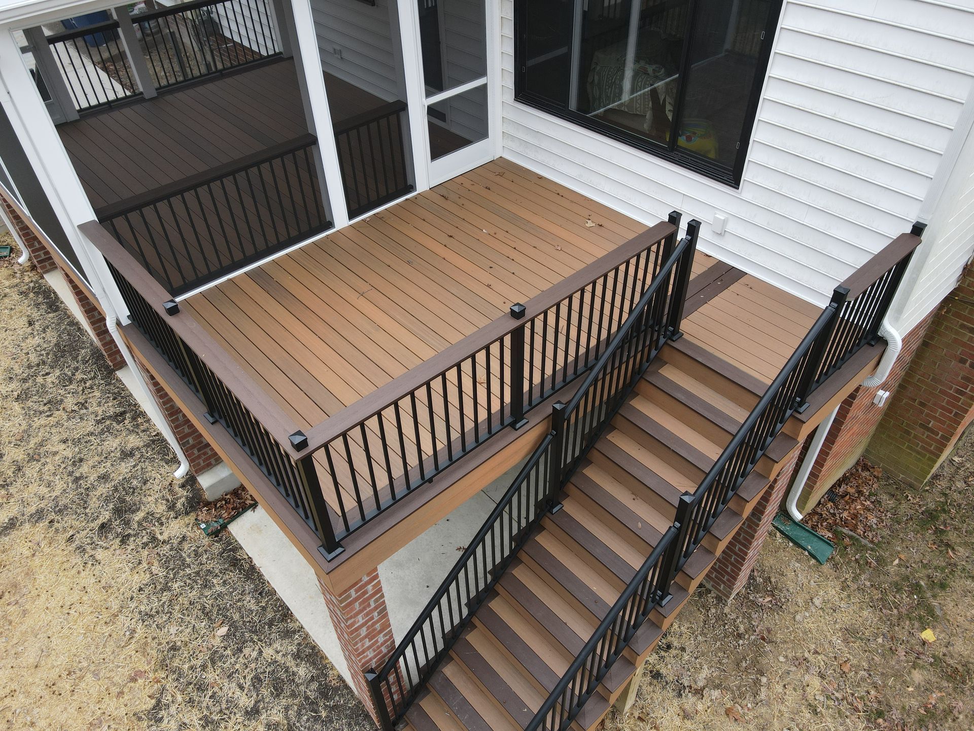 Front porch with wooden deck and black railings beside white siding and steps leading down to a lower landing
