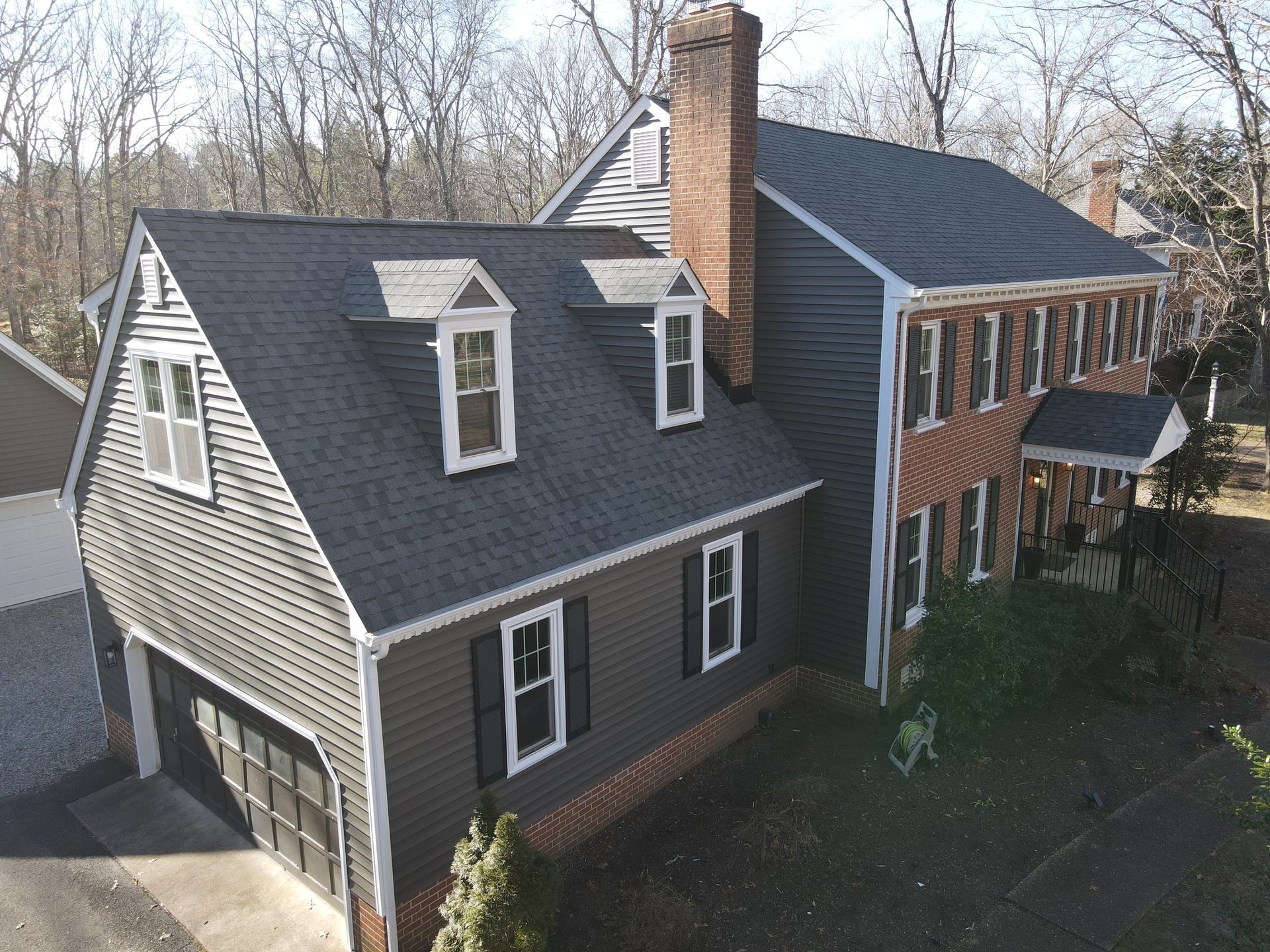 Aerial view of a two-story house with dark shingles, brick and gray siding, and a chimney.
