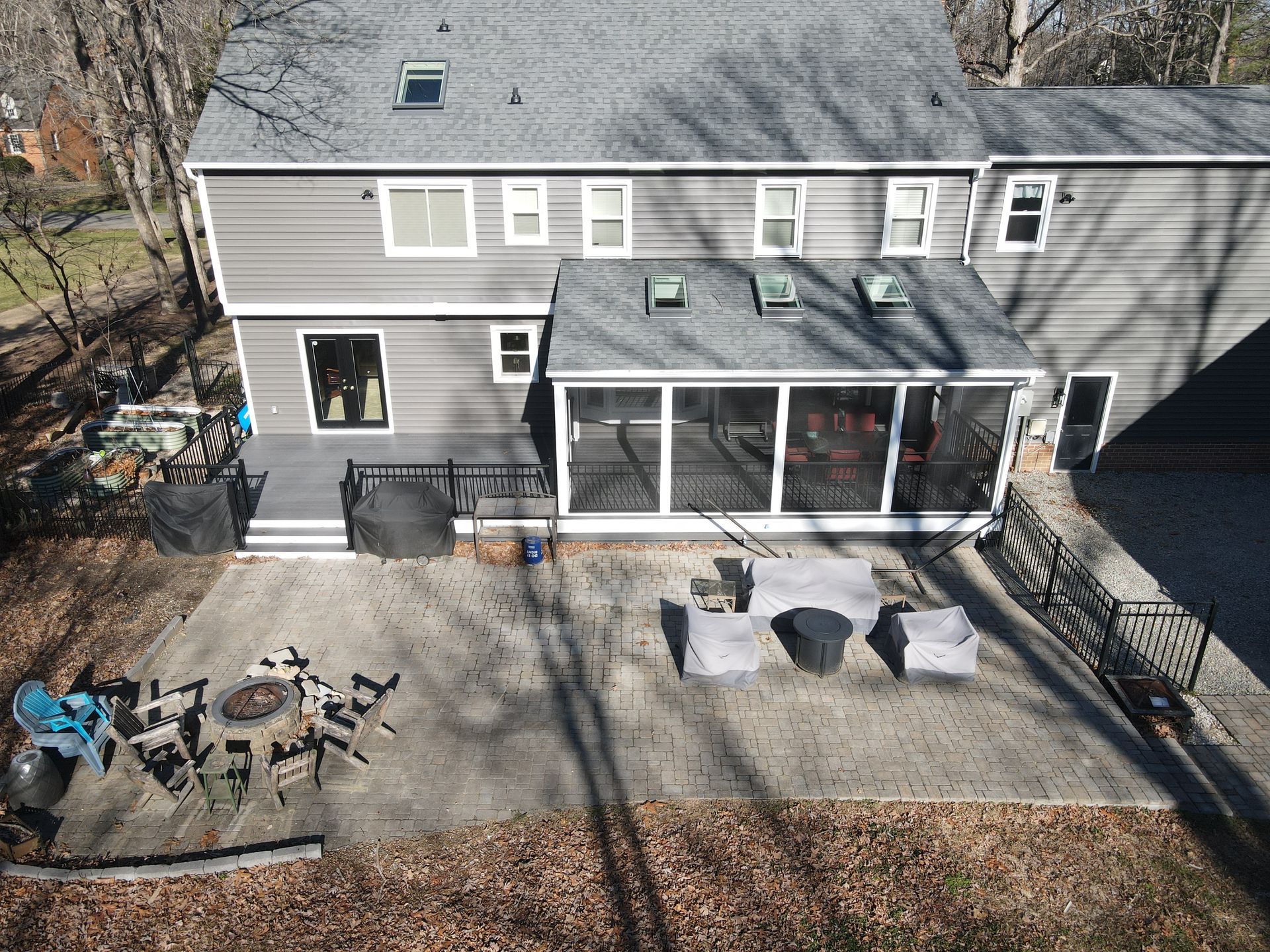 Aerial view of a gray two-story house with a screened porch and patio furniture in the backyard.