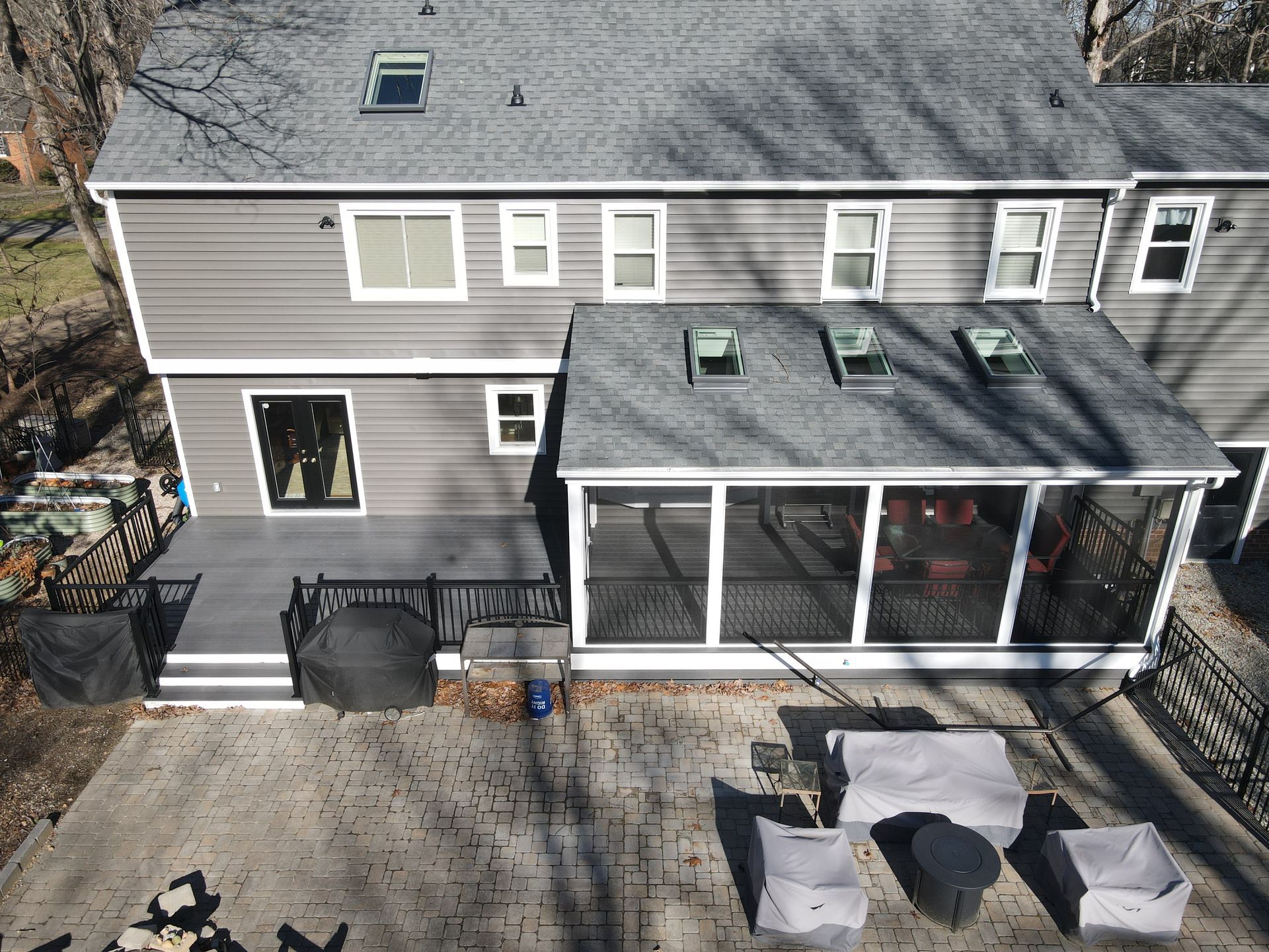 Gray two-story house with screened porch, patio seating, and a paved driveway in front