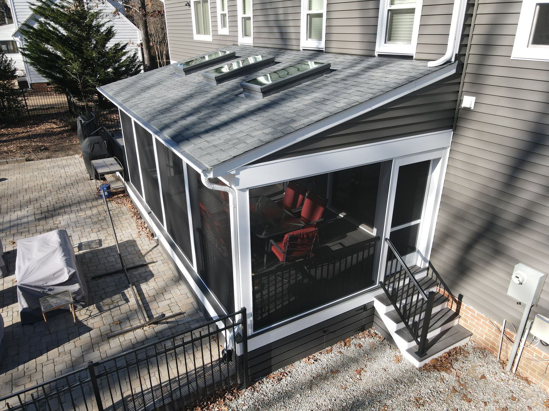 Small screened porch with black railing and red chair beside a beige house, viewed from outside