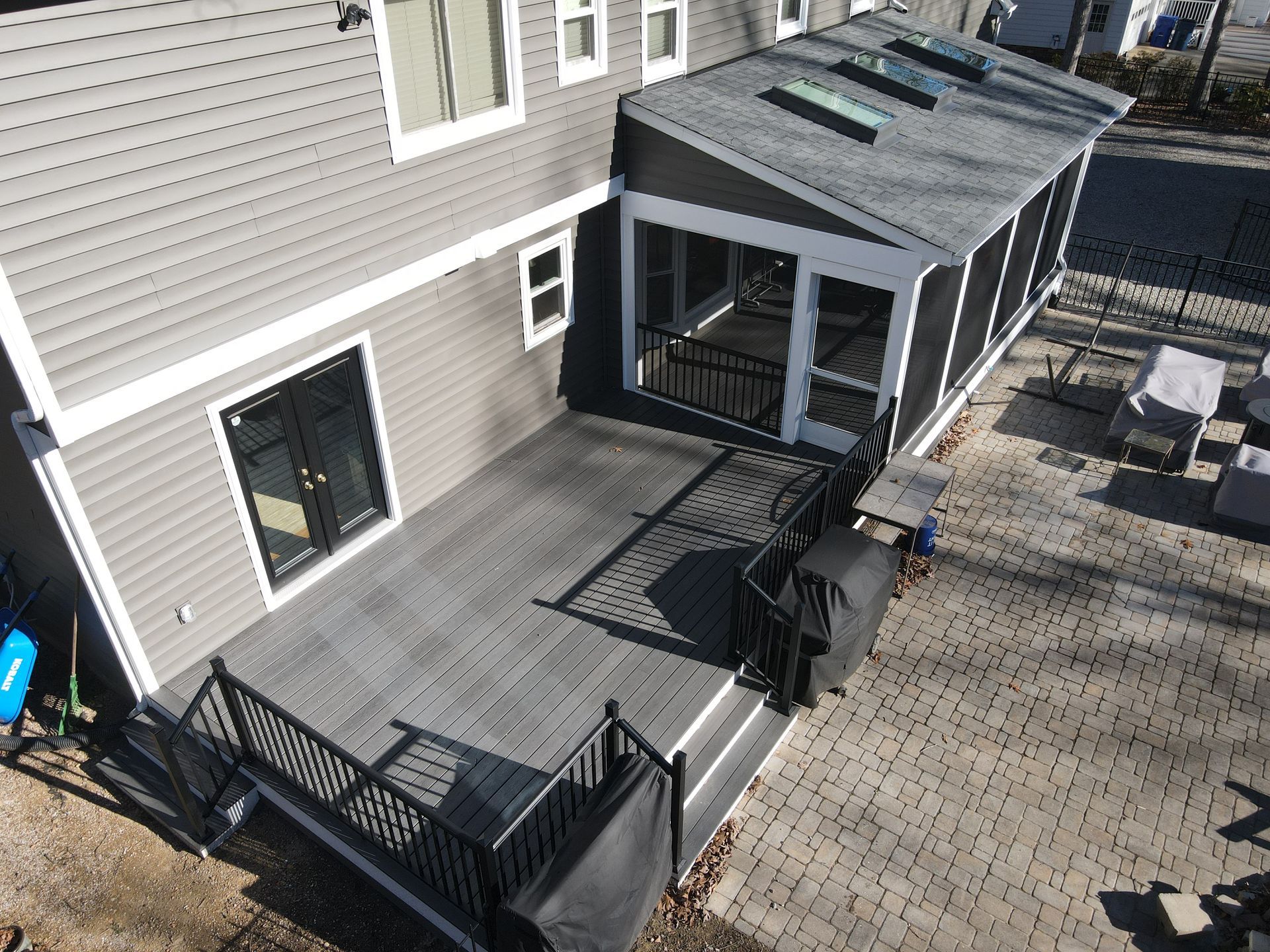 Backyard deck and screened porch beside a beige house, with black railings and outdoor furniture.