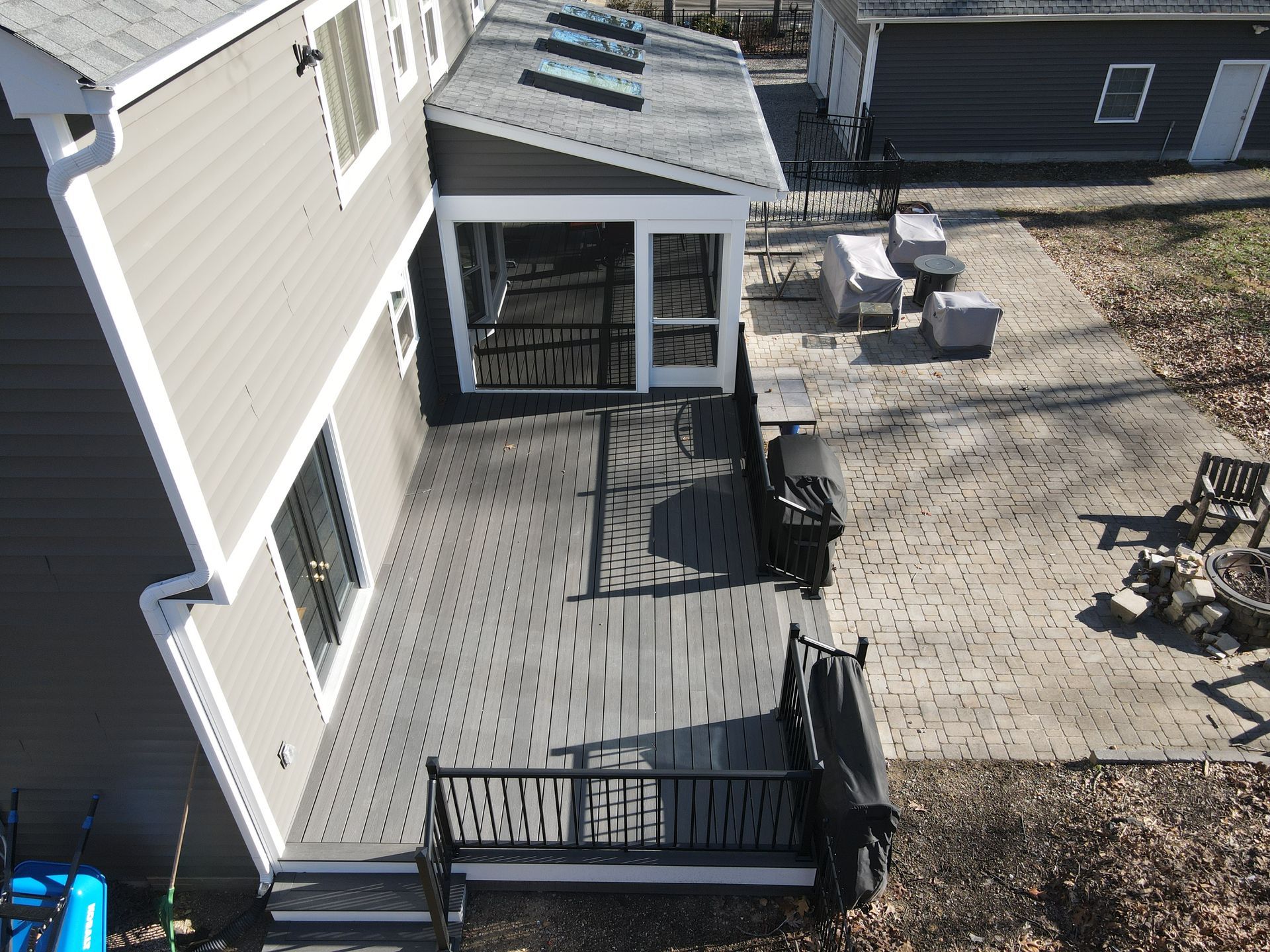 Deck and patio beside a beige house with black railings, a small covered porch, and outdoor furniture
