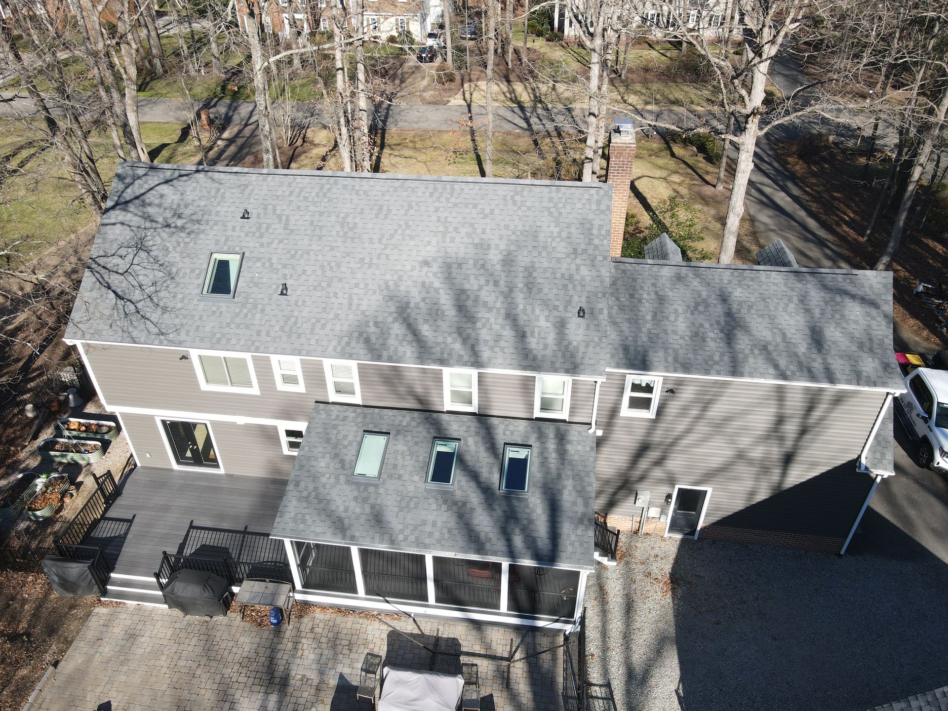 Aerial view of a gray two-story house with a dark roof and screened porch, surrounded by bare trees.