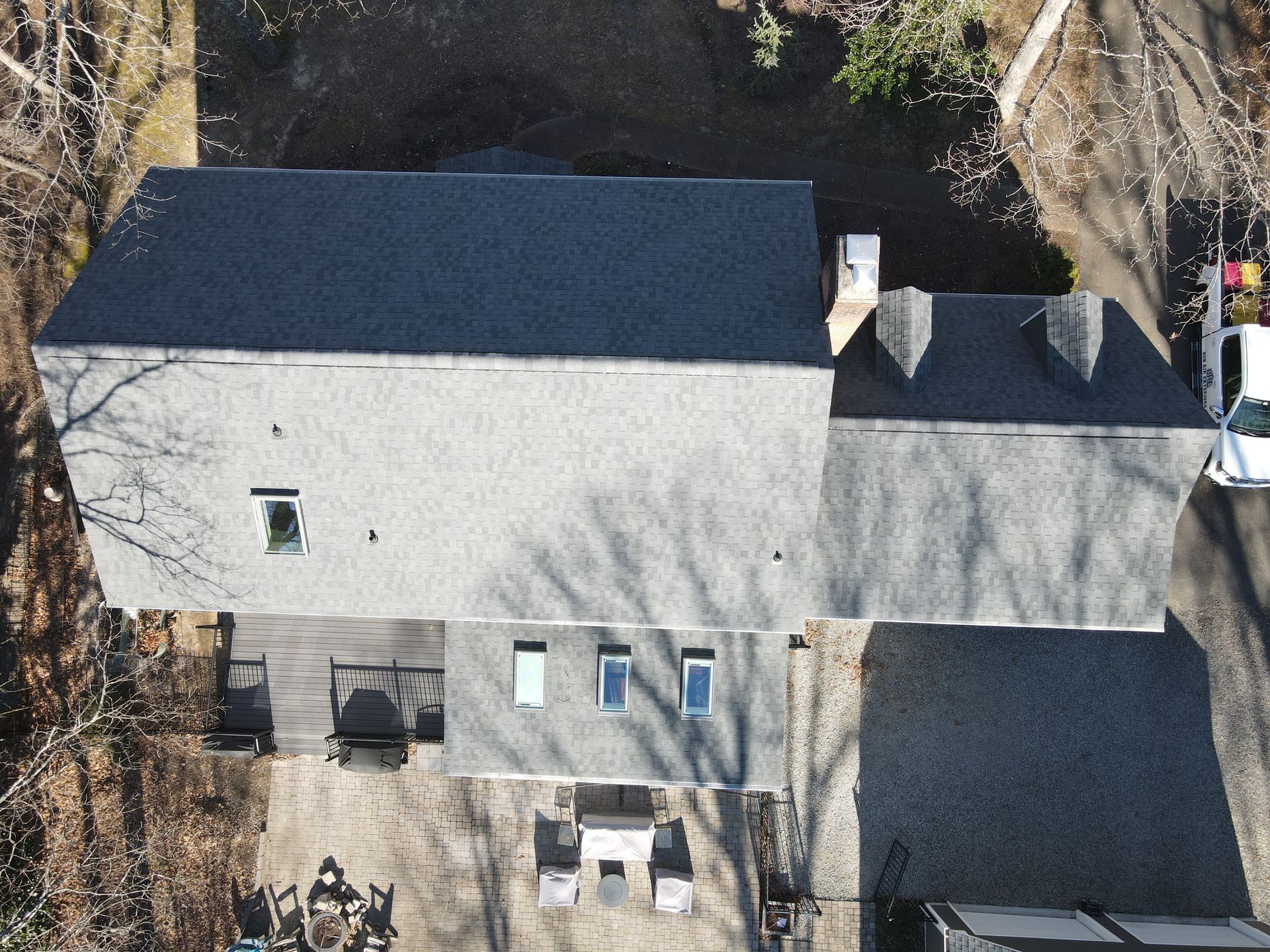 Aerial view of a gray-roofed house with a smaller attached roof and trees around it.