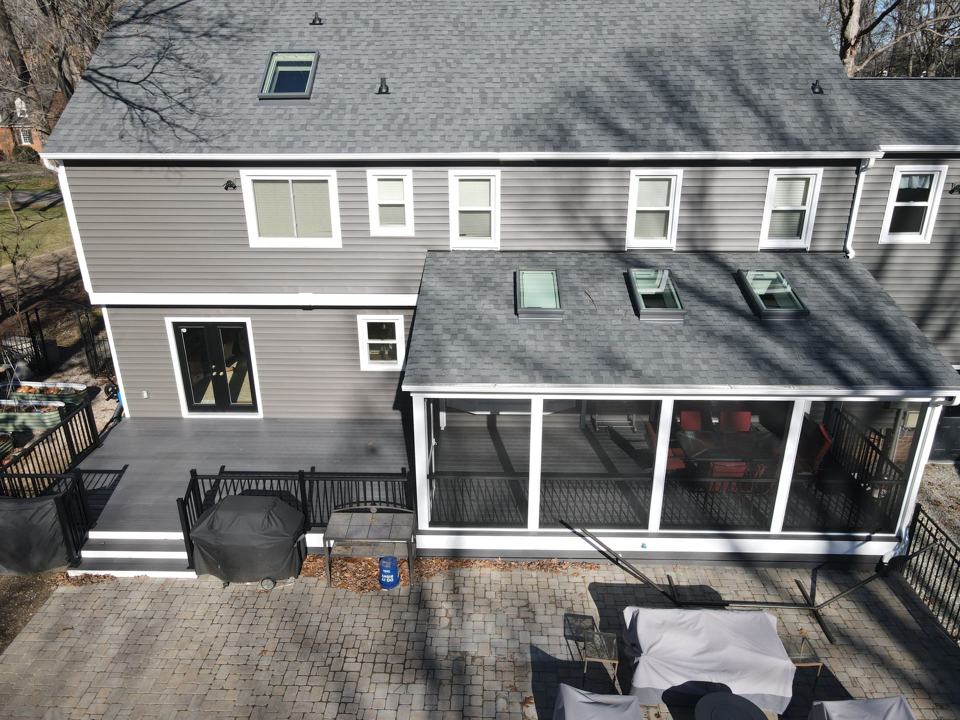 A gray two-story house with a screened porch and deck, viewed from above in winter.