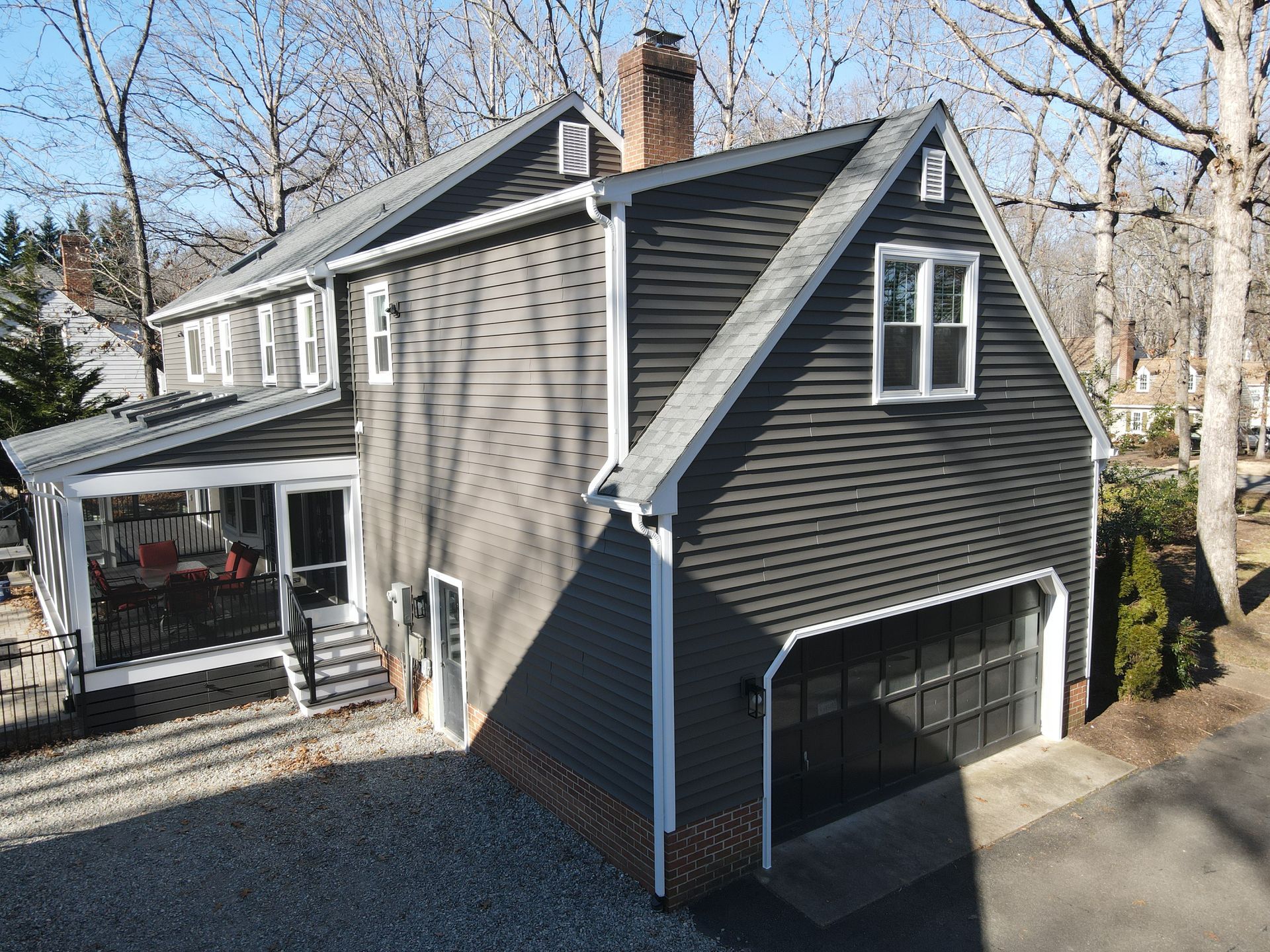 Gray two-story house with attached garage, white trim, and covered porch in a wooded yard.