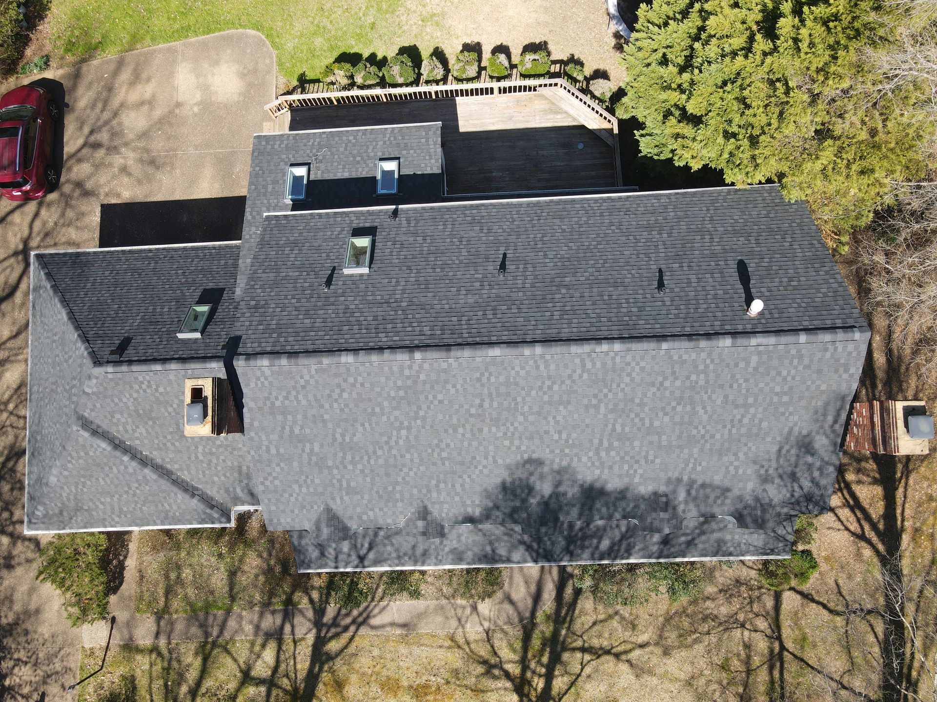 Aerial view of a gray-shingled house with a driveway, yard, and trees around it.