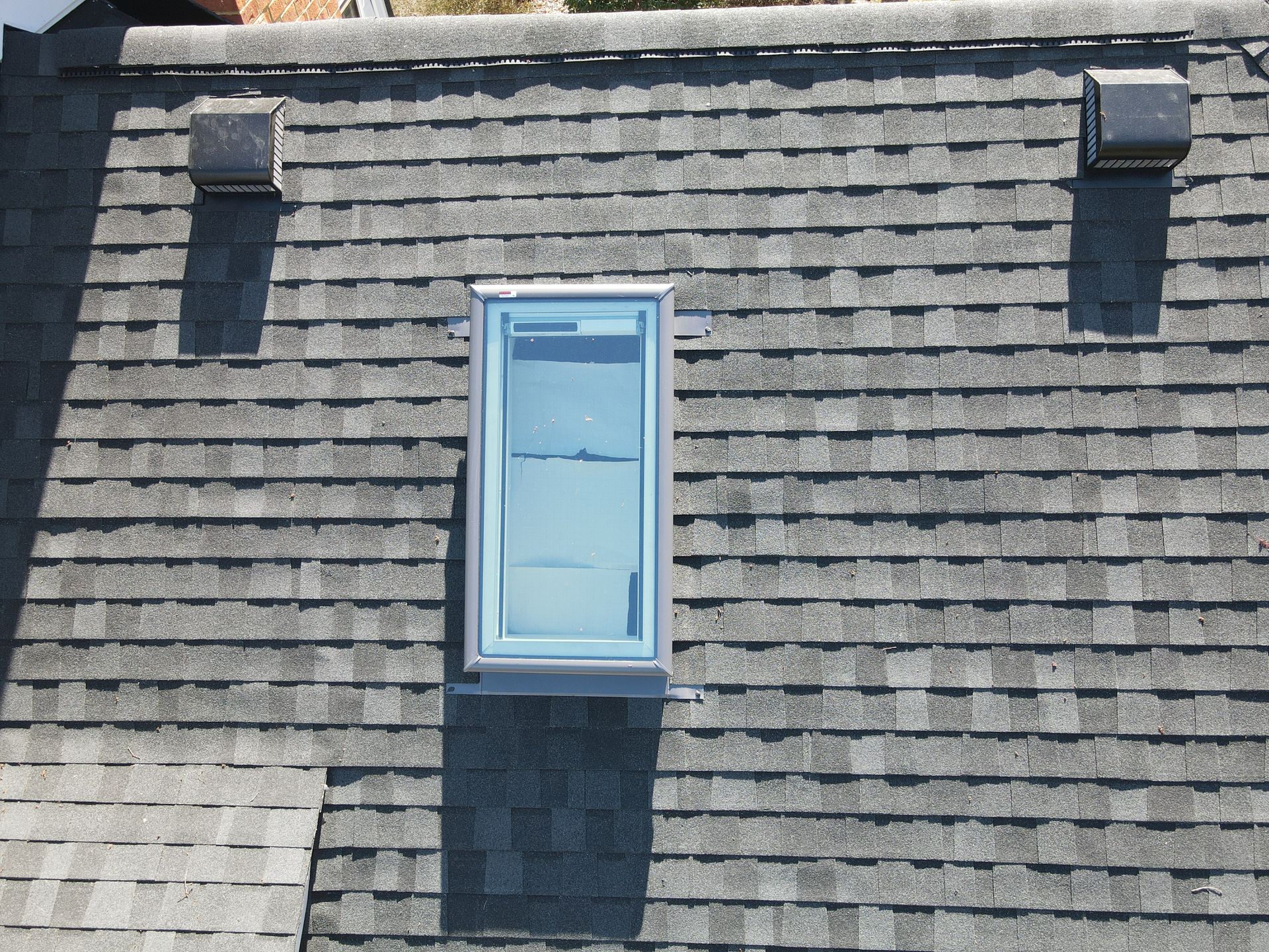 Roof with gray shingles and a small blue-framed skylight window.
