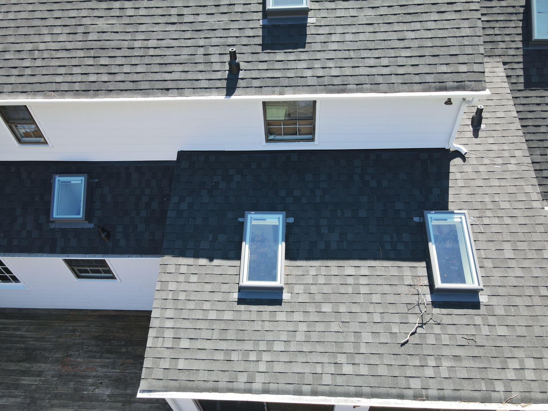 Roof with gray shingles, dormer windows, and a white side wall on a house.