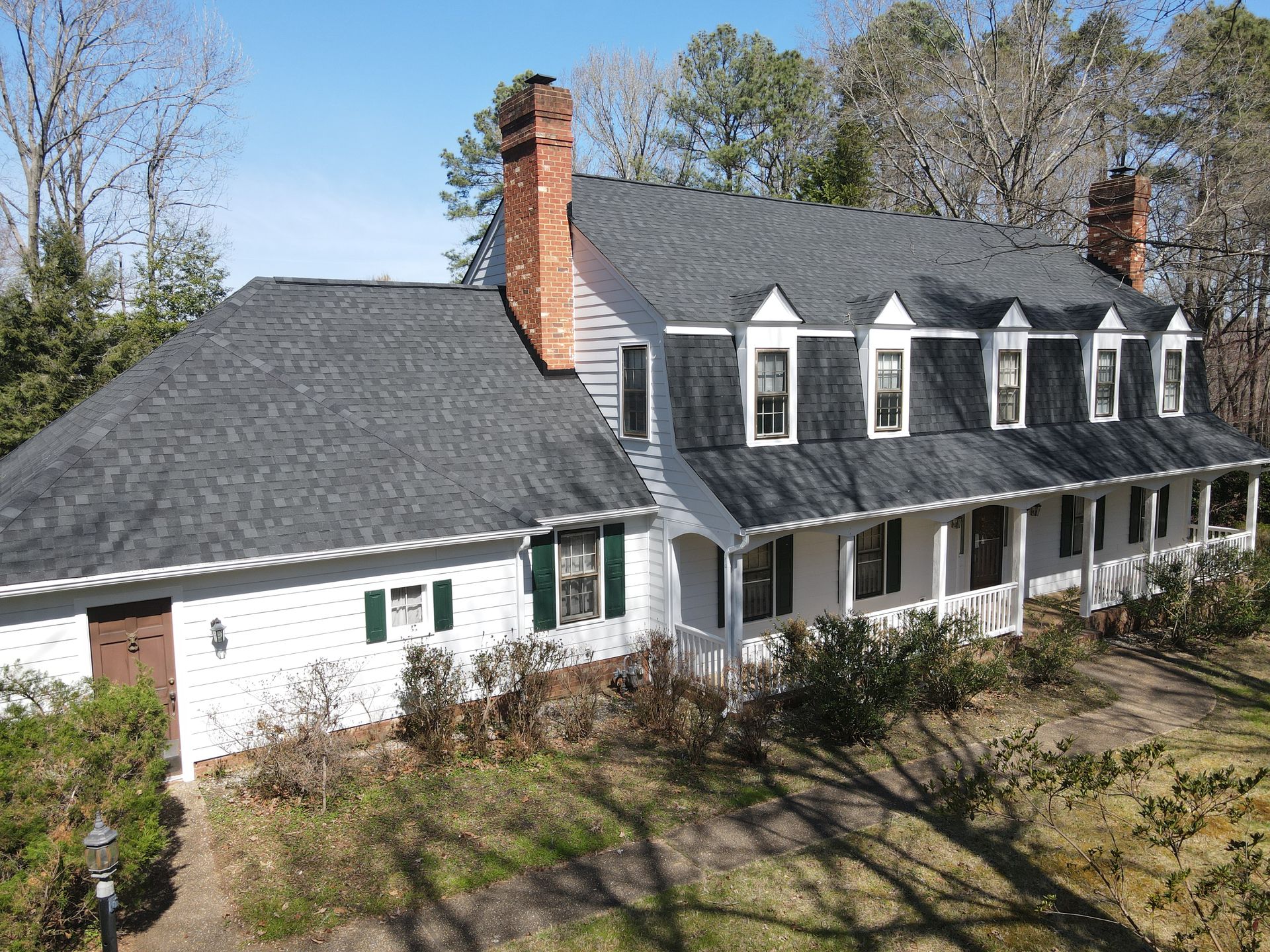 Large white house with dark gray roof and red brick chimneys, viewed from above on a sunny day.