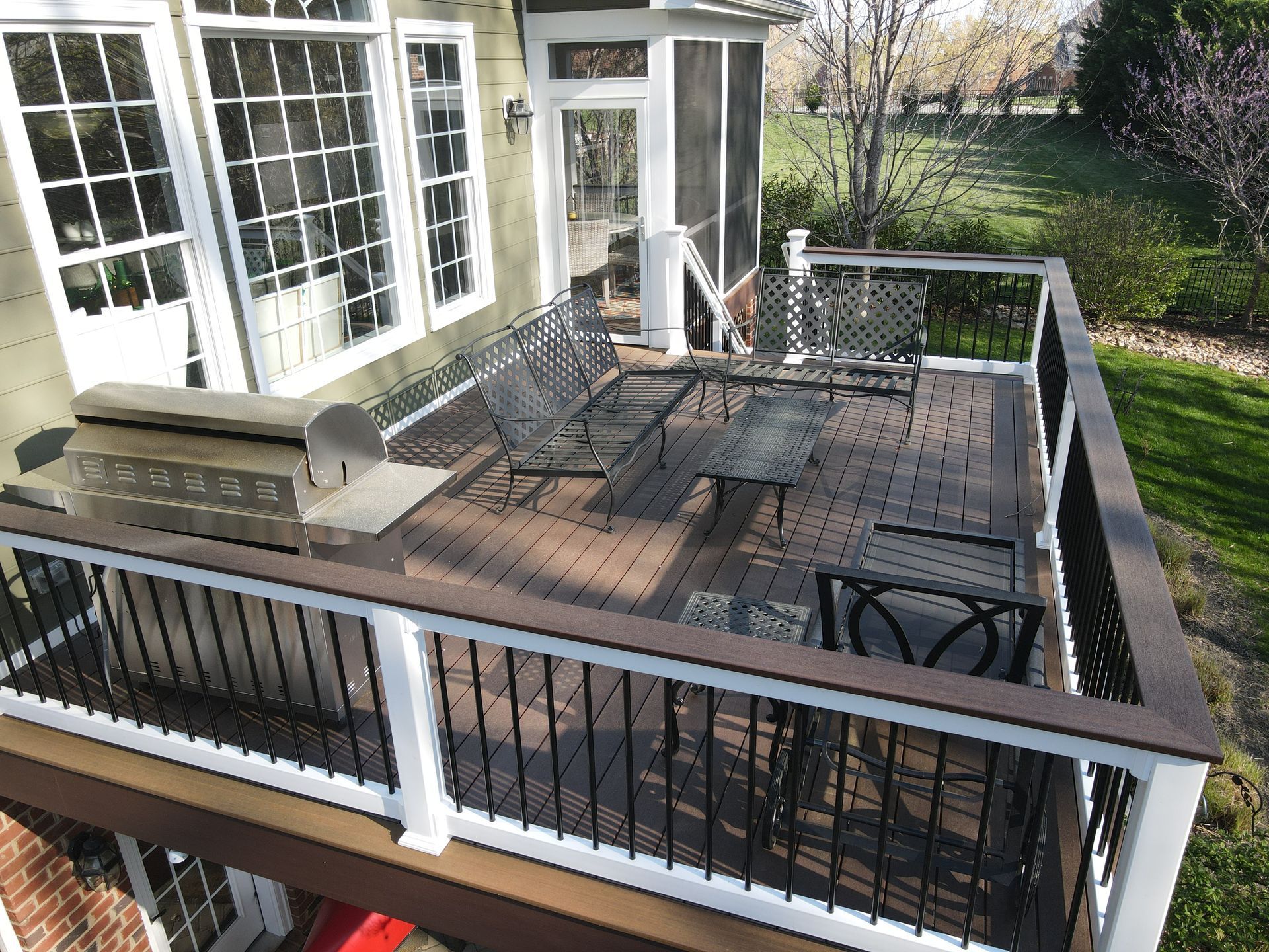 Wooden patio deck with black railing, outdoor seating, and white house doors overlooking a grassy yard