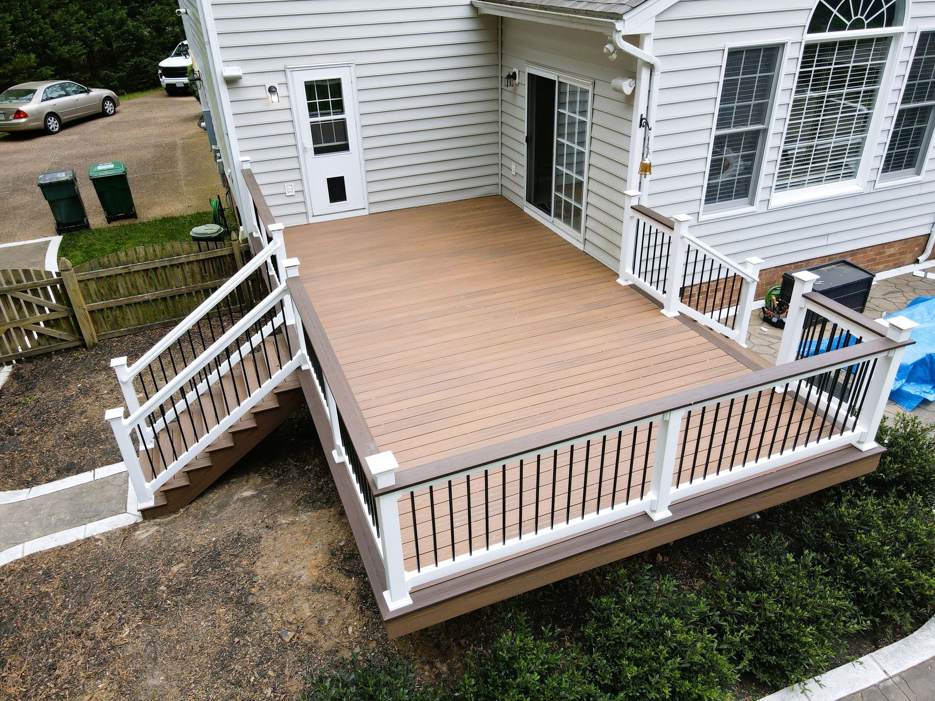 Back deck with light wood floor, white railings, and stairs leading to a sliding glass door