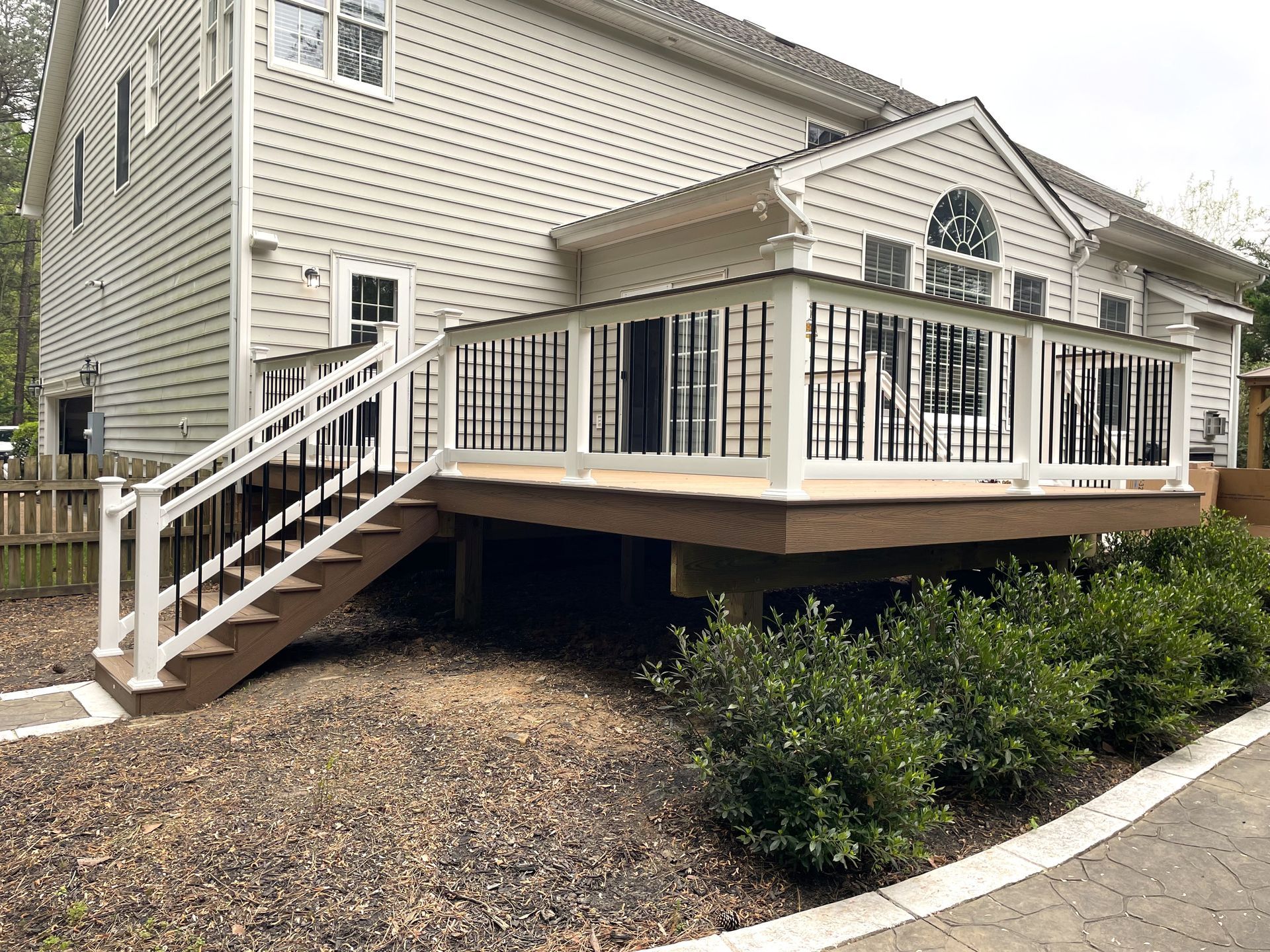 Raised wooden deck with white railings and stairs beside a beige house.