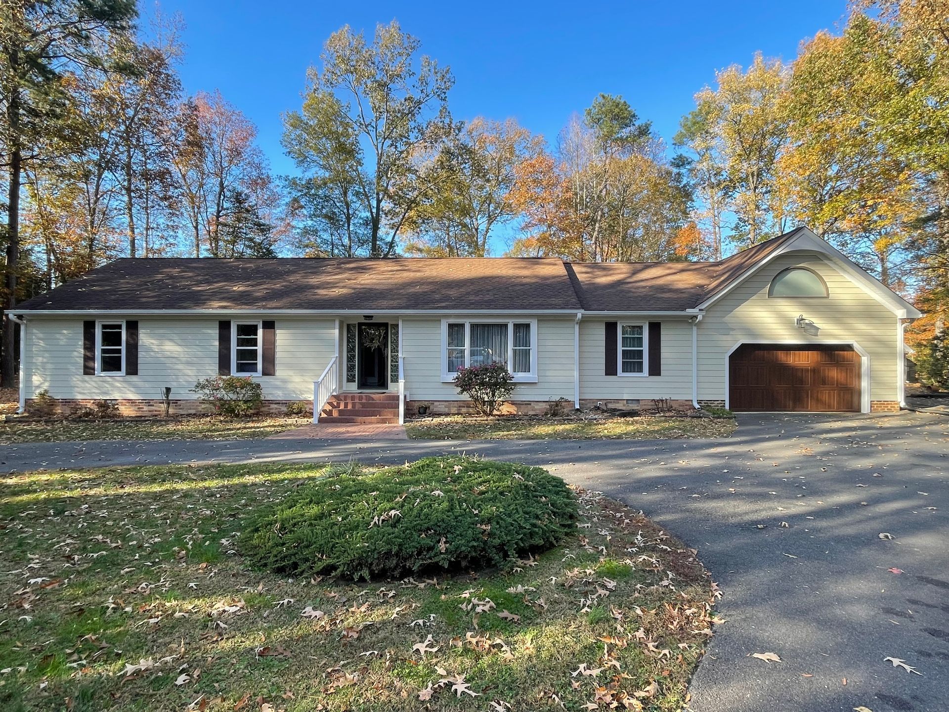 Single-story white house with attached garage, front porch, and autumn trees in the yard