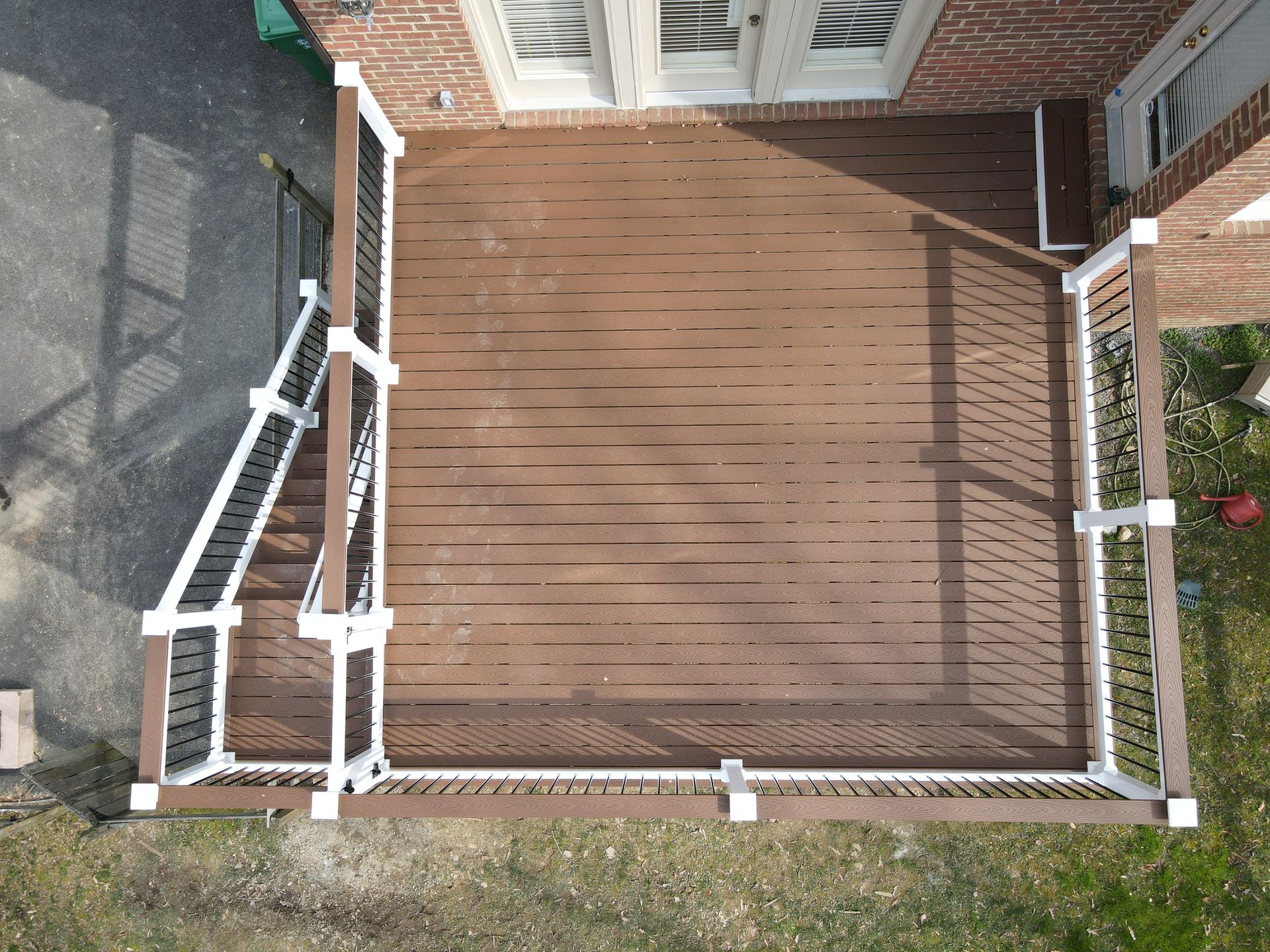 Top-down view of a wooden backyard deck with white railings beside a brick house.