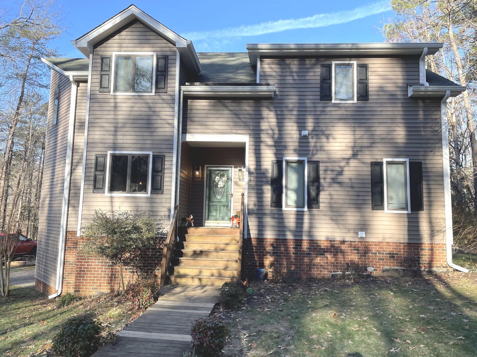 Two-story beige house with brick base, front walkway, and green door in a wooded yard